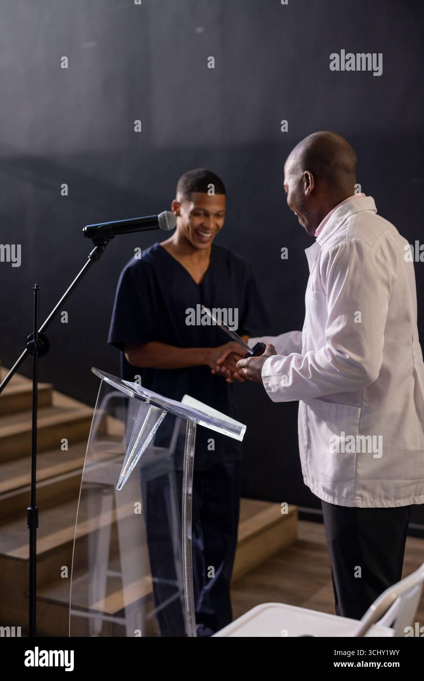 Ein Mann, der auf der Bühne ausgezeichnet wurde, lächelt und dem Moderator die Hand schüttelt Stockfoto