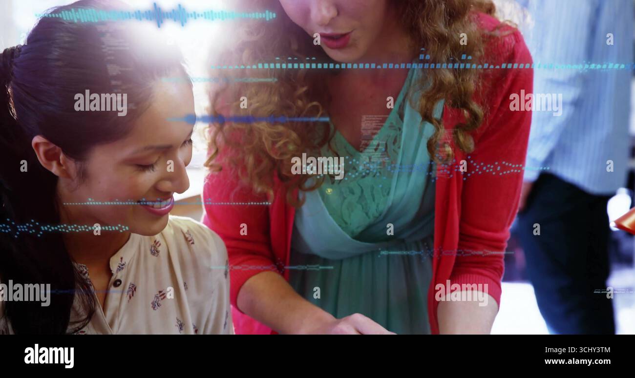Frauen, die über ein Tablet am hellen Schreibtisch arbeiten, auf den Bildschirm und Dokumente zeigen Stockfoto
