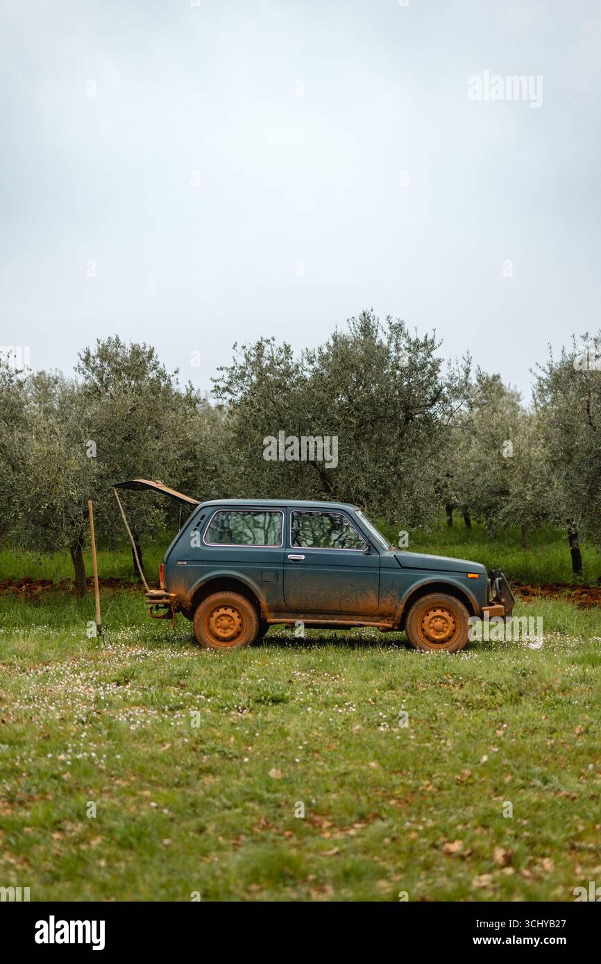 Lada Niva Geländewagen in einem Olivenhain, historisches landwirtschaftliches Fahrzeug in ländlichen Gebieten, mit Schlamm auf Rädern und natürlicher Landschaft. Stockfoto