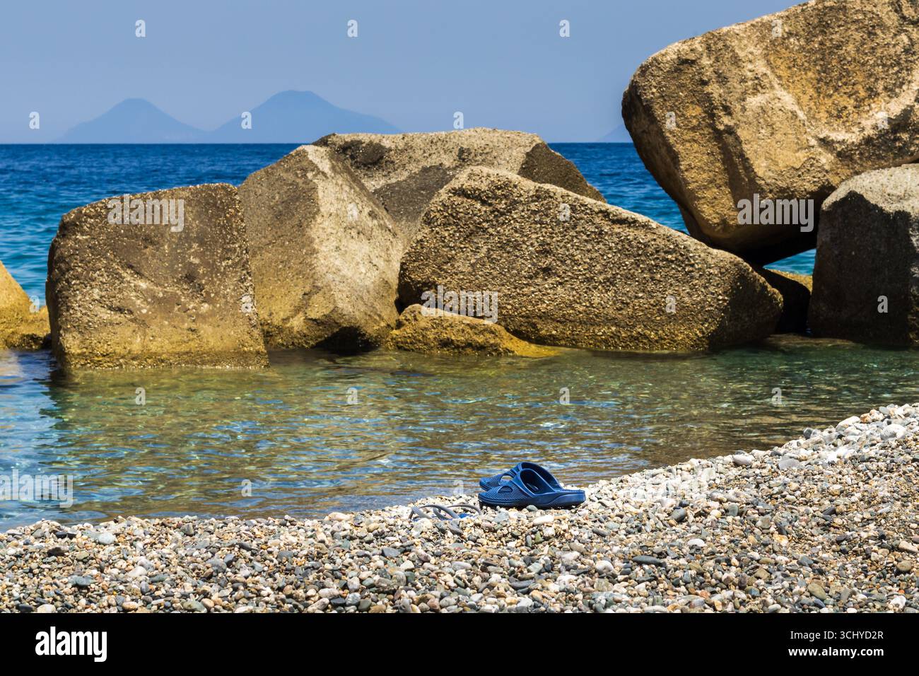 Strandschuhe vor dem Meer und den Felsen Stockfoto