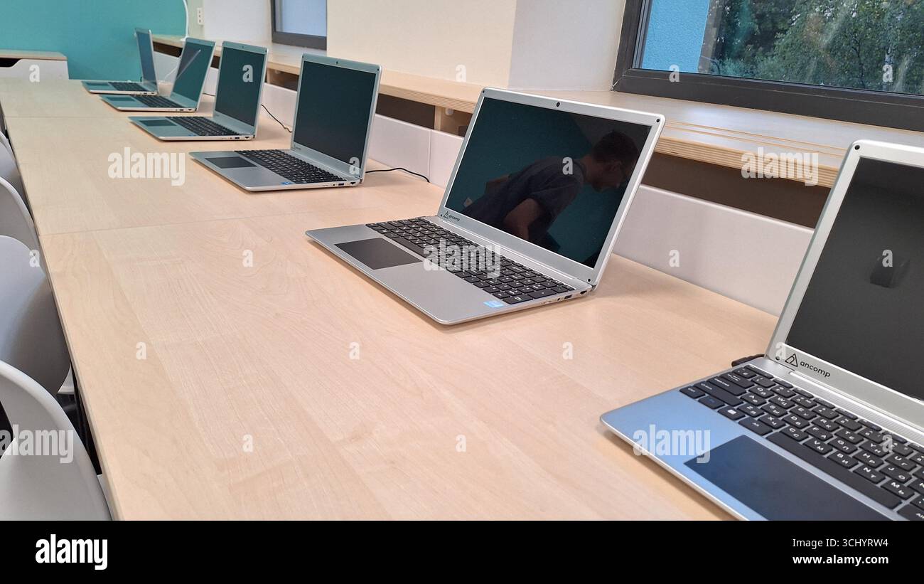 Moskau , Russland - 27. August 2025.Reihe von Laptops auf dem Schreibtisch im Klassenzimmer mit Reflexion in moderner Bildungsumgebung Stockfoto