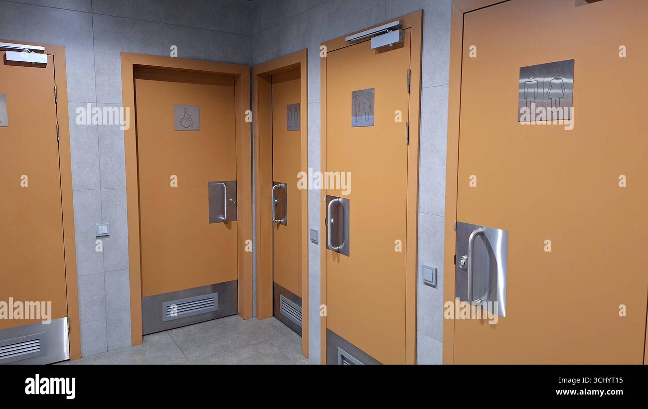 Orangefarbene Toilettentüren mit Hinweisschildern in modernen öffentlichen Einrichtungen Stockfoto