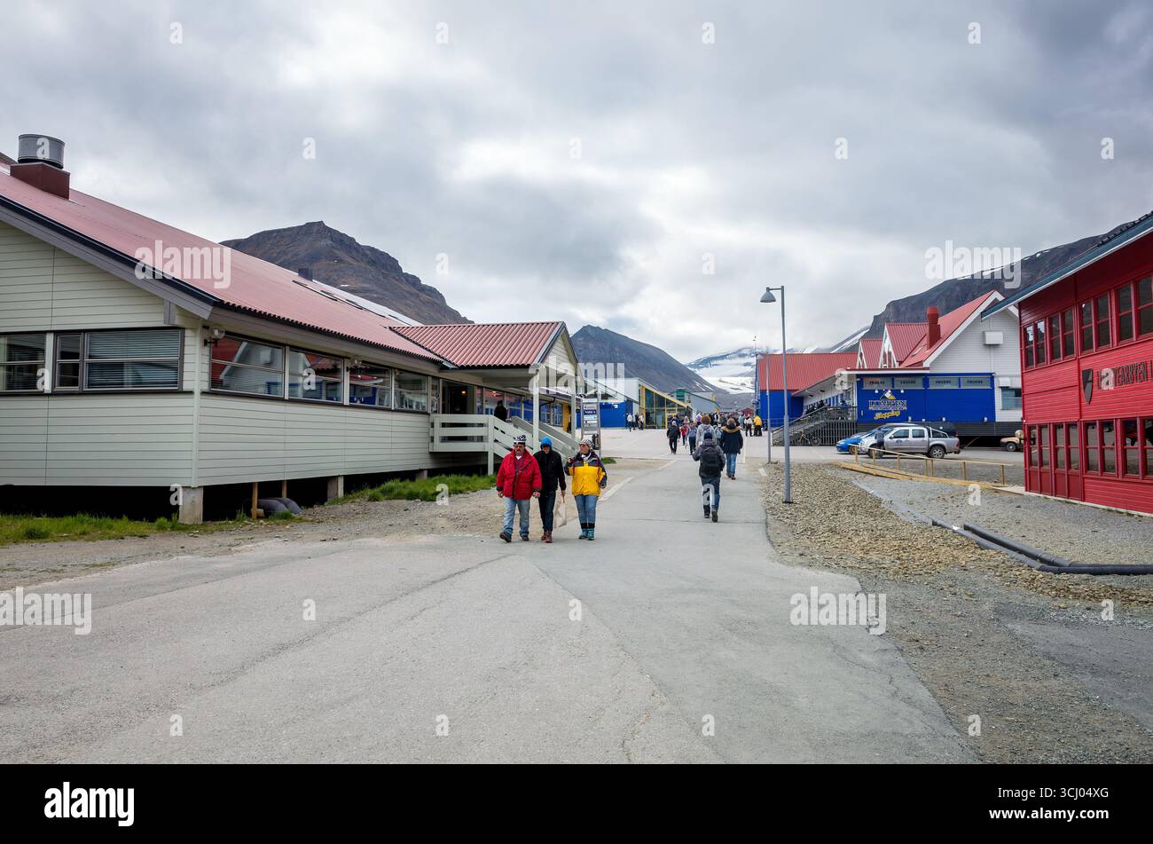 Longyearbyen Hotel Longyearbyen Svalbard Norwegen // LONGYEARBYEN, Svalbard und Jan Mayen – die Menschen laufen entlang einer Straße, die von bunten Gebäuden gesäumt ist, in Longyearbyen, der größten Siedlung auf dem Svalbard-Archipel. Die Stadt liegt in einem Tal mit steilen, schneebedeckten Bergen im Hintergrund unter bewölktem Himmel. Longyearbyen ist die nördlichste Stadt der Welt und dient als Verwaltungszentrum der Region Svalbard. Die Architektur verfügt über farbenfrohe Holzkonstruktionen, die typisch für arktische Siedlungen sind, um widrigen Wetterbedingungen standzuhalten. Stockfoto