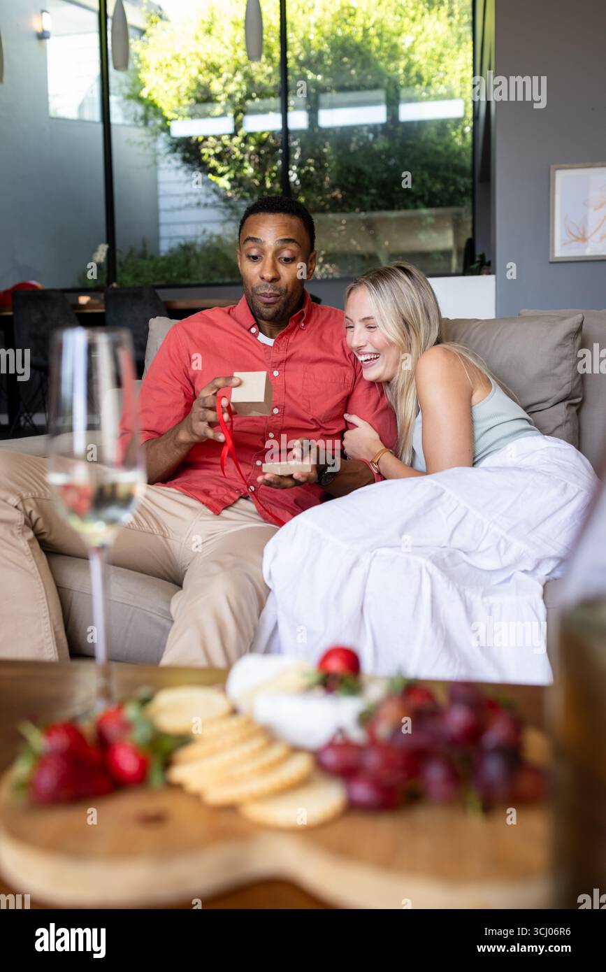 Verschiedene Paare auf der Couch tauschen Geschenke aus, genießen gemütliche Feierlichkeiten zu Hause Stockfoto