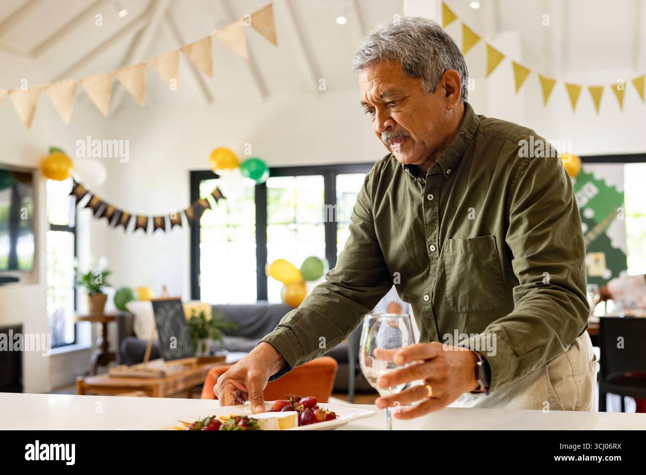 Senior Mann, der Essen zubereitete und Weinglas auf festlicher Hausfeier hielt Stockfoto