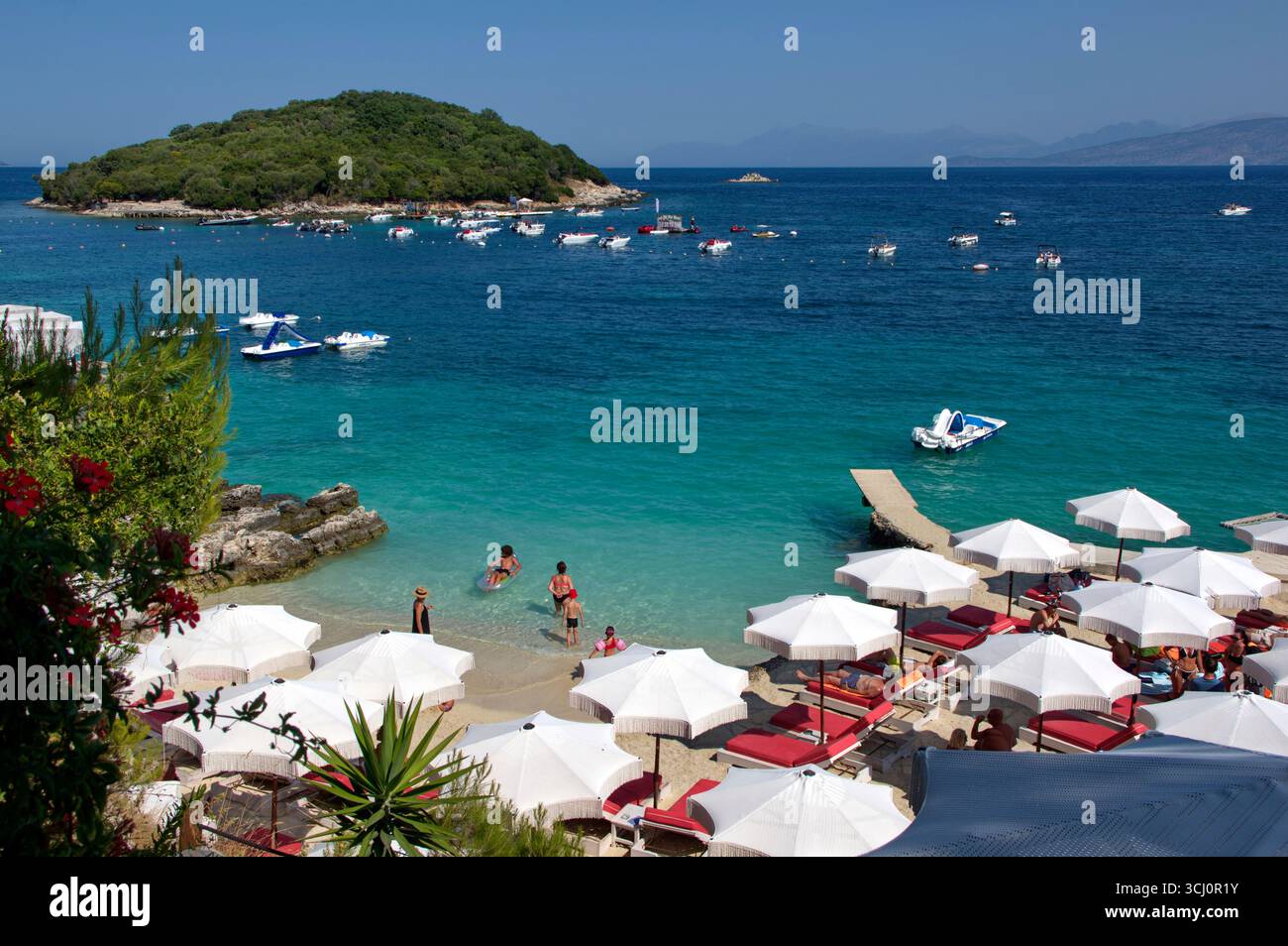 Panoramica di una spiaggetta a Ksamil complete amente occupata da ombrelloni e lettini e del Mare azzurro alle spalle Stockfoto