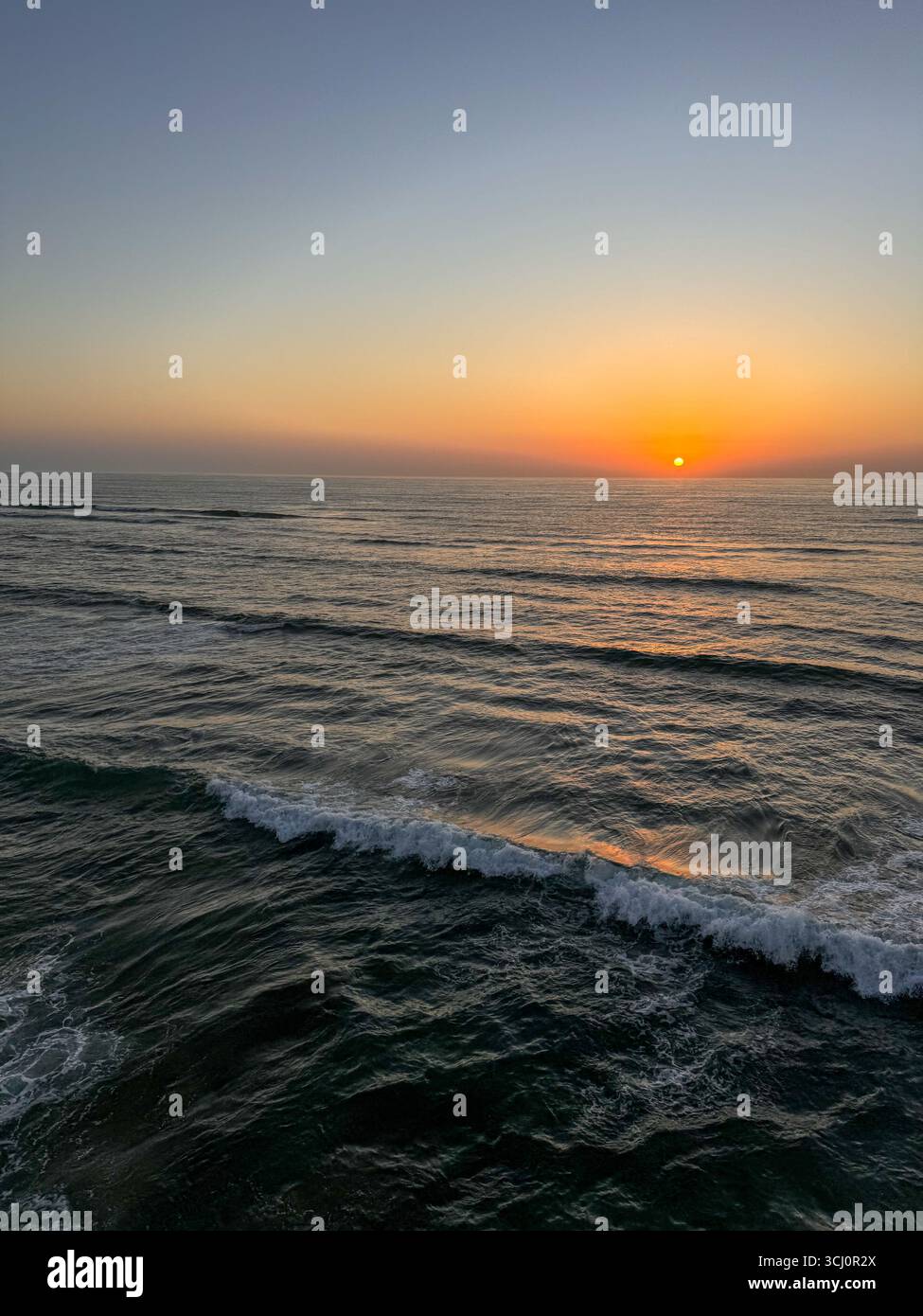 Farbenfroher Sonnenuntergang über dem Atlantischen Ozean mit Wellen und einem klaren Horizont. - Smartphone-aufgenommenes Stockfoto