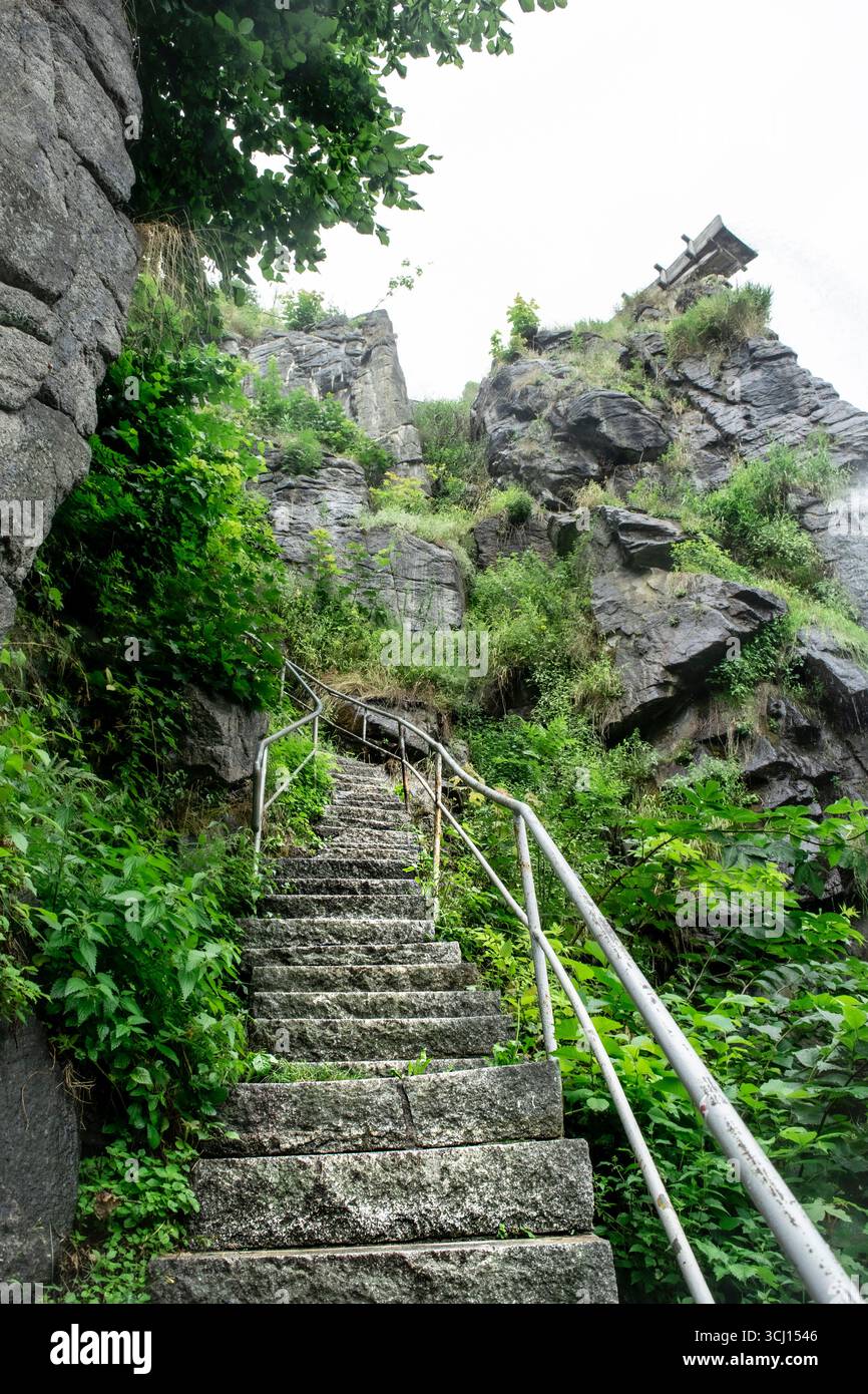 Eine verwinkelte Steintreppe erhebt sich auf eine zerklüftete, moosbedeckte Klippe. Diese leistungsstarke Grafik symbolisiert eine anspruchsvolle Reise, einen Weg zum Erfolg. Stockfoto