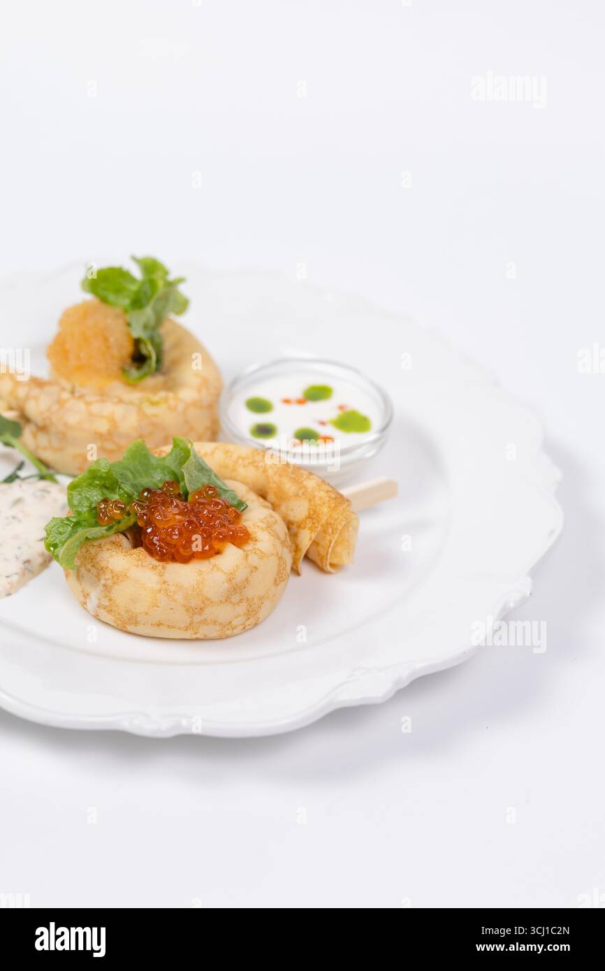Elegantes Servieren von Gourmet-Pfannkuchen mit rotem Kaviar, frischem Salat, Cremesauce und Kräutern auf einem weißen Teller für das Restaurantmenü. Stockfoto