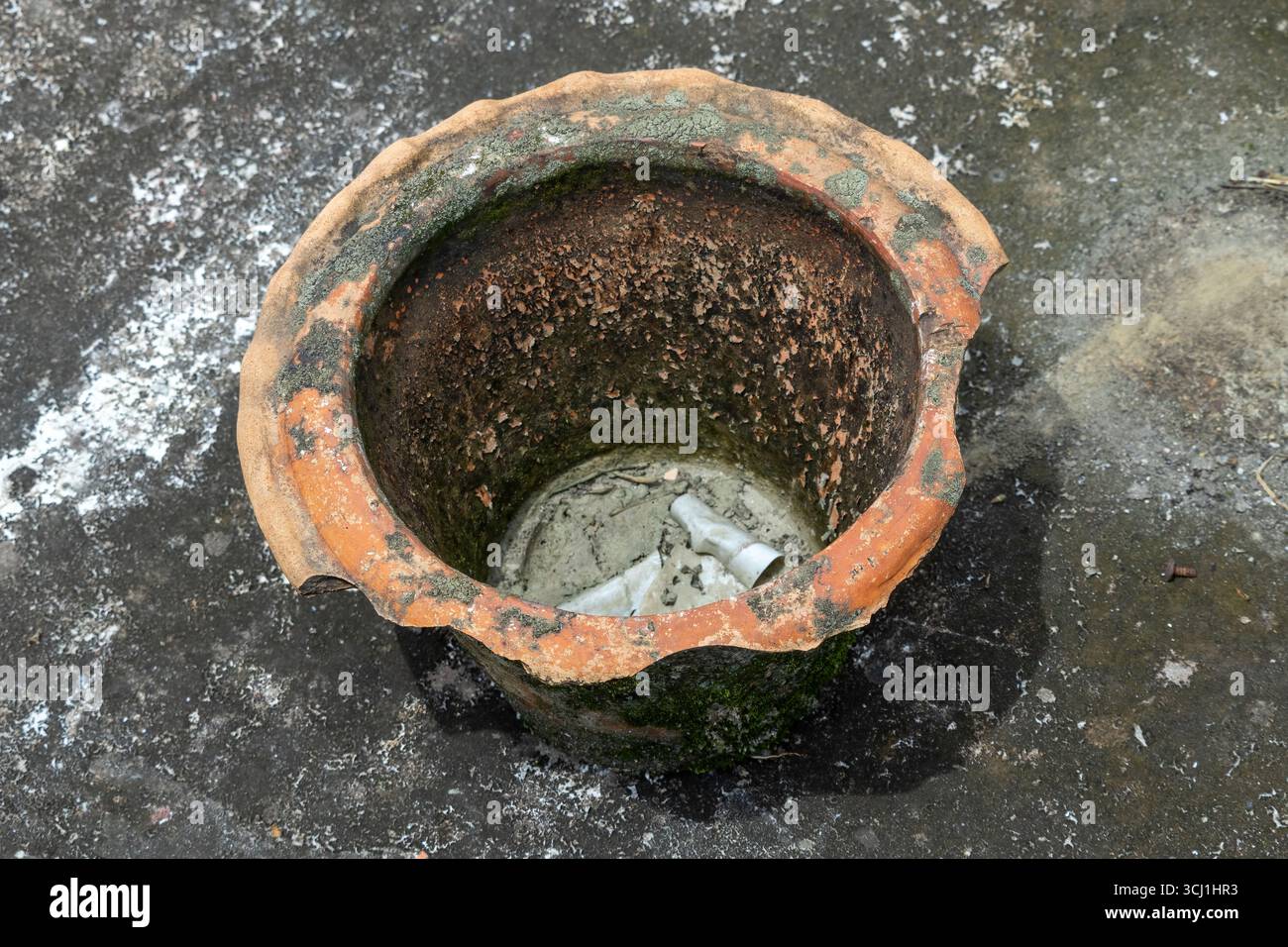 Ein alter, leerer und kaputter Blumentopf sitzt auf einem verwitterten Betondach und symbolisiert die Vernachlässigung des Gartens. Stockfoto