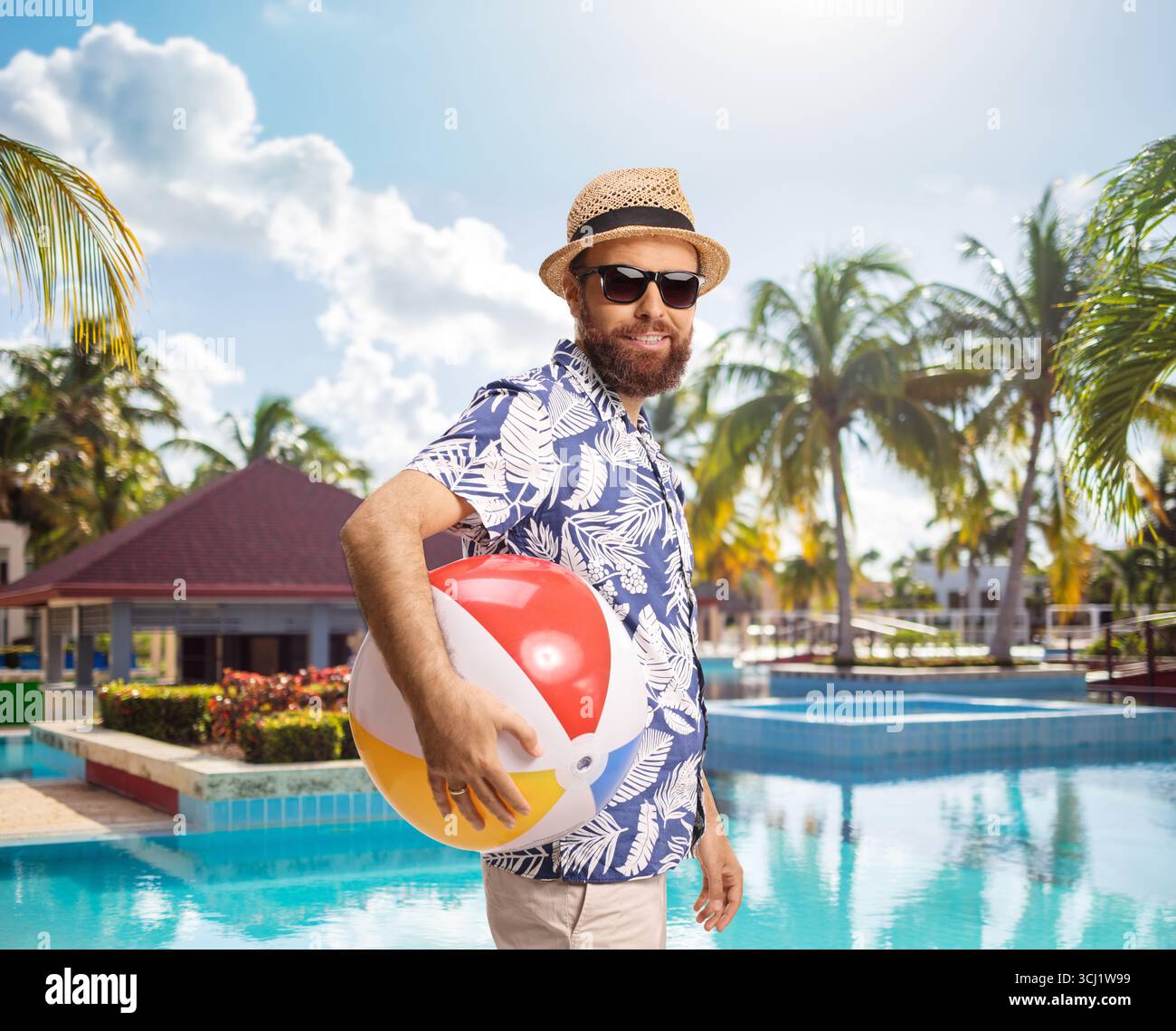 Bärtiger Mann mit Sonnenbrille, der einen Strandball in der Nähe eines Schwimmbades hält Stockfoto