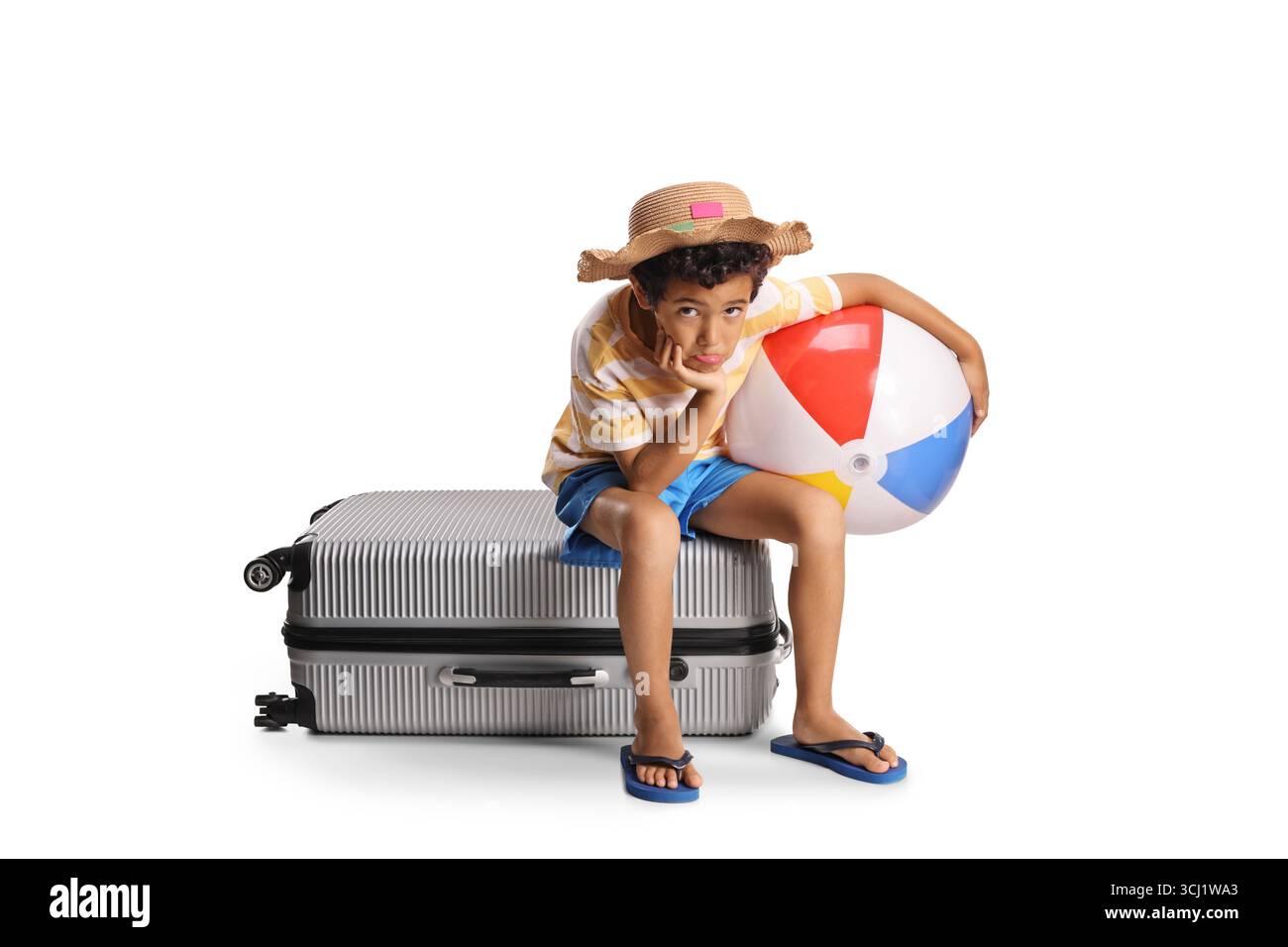 Junge, der auf einem Koffer sitzt und einen Strandball auf weißem Hintergrund hält Stockfoto
