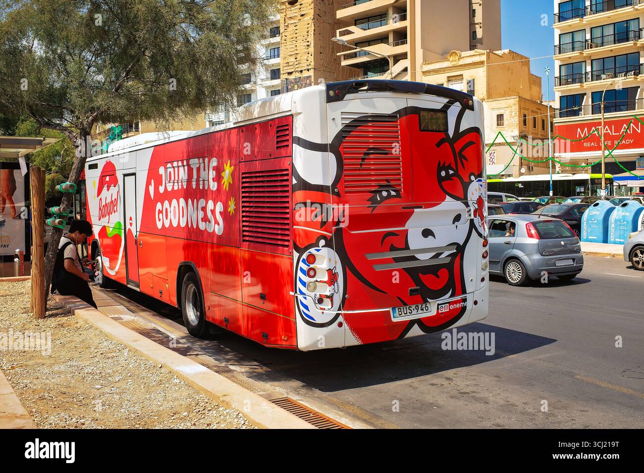 Sliema, Malta - 26. August 2025: Stadtbus mit Babybel-Werbung und Kuhillustration parkt auf der Straße zwischen Gebäuden und Autos Stockfoto
