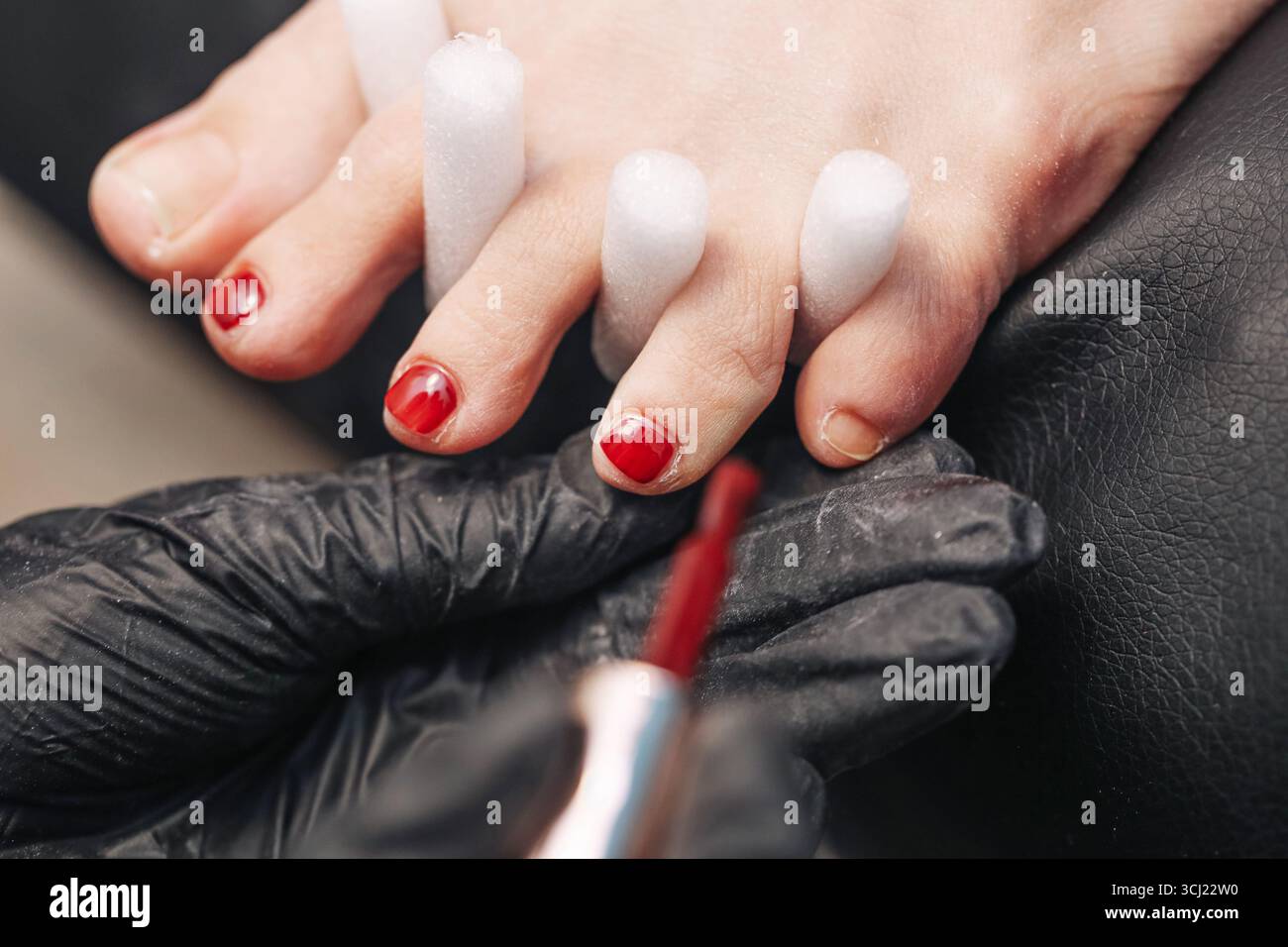 Professionelle Pedikürbehandlung. Weibliche Zehen mit rotem nagellack. Schönheitssalon Fußpflege-Nahaufnahme. Nagelstylist arbeitet mit Bürste. Stockfoto
