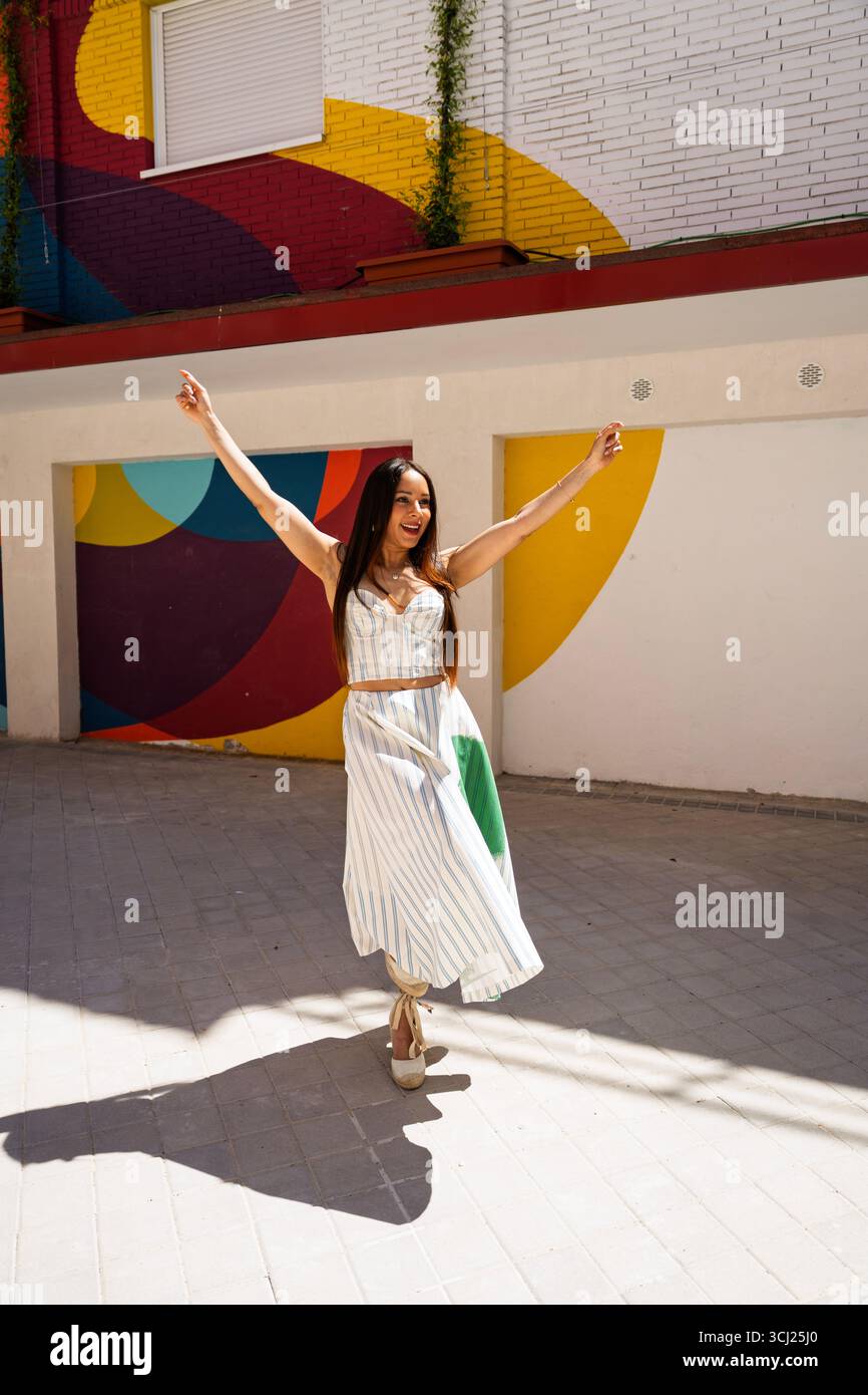 Sorglose junge Frau, die mit erhobenen Armen vor lebendiger Straßenkunst tanzt und die Sommerstimmung genießt Stockfoto