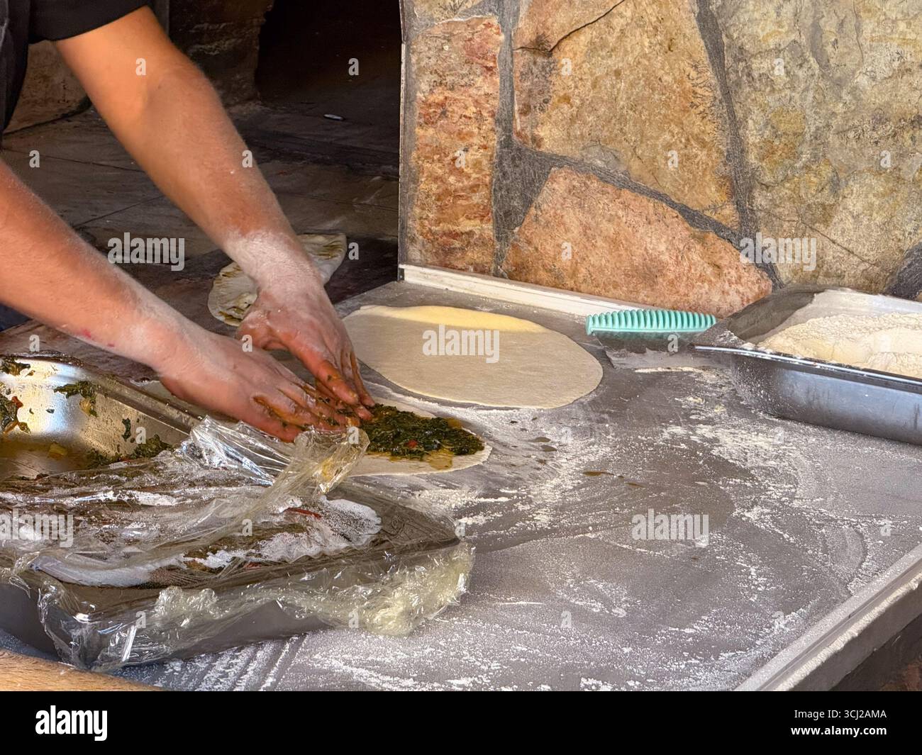 Hände, die Fladenbrot mit Gemüsefüllung auf einer bemehlten Oberfläche zubereiten. Traditionelle Küche, Küche und Gastronomie durch handgemachtes Brot Stockfoto