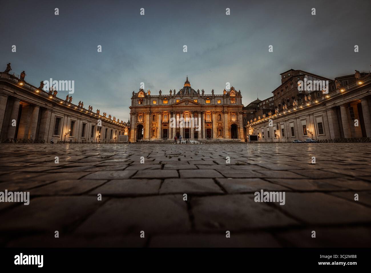 Ein niedriger Blickwinkel fängt die beeindruckende Fassade des Petersdoms im Vatikan in der Dämmerung ein. Die warmen Lichter beleuchten die prächtige Bar Stockfoto