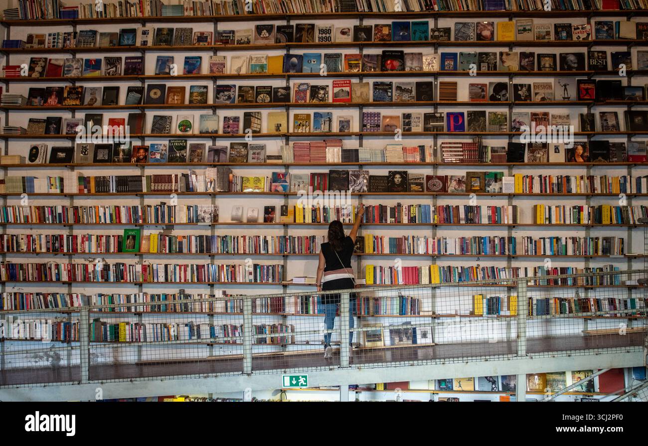 Ein Mensch greift nach einem Buch in einem riesigen, mehrstöckigen Buchladen. Das Bild zeigt die unglaubliche Größe des Bücherregals, das vom Boden bis zur Decke gefüllt ist Stockfoto
