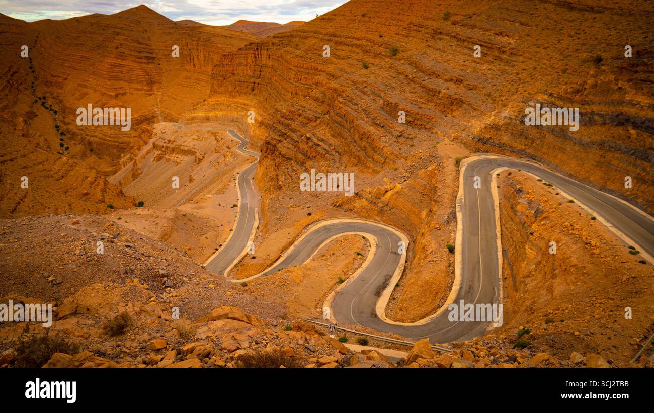 Dades Gorge in Marokko mit gewundenen Bergstraßen, die sich durch dramatische felsige Schluchten und steile Klippen unter bewölktem Wüstenhimmel kurvieren Stockfoto