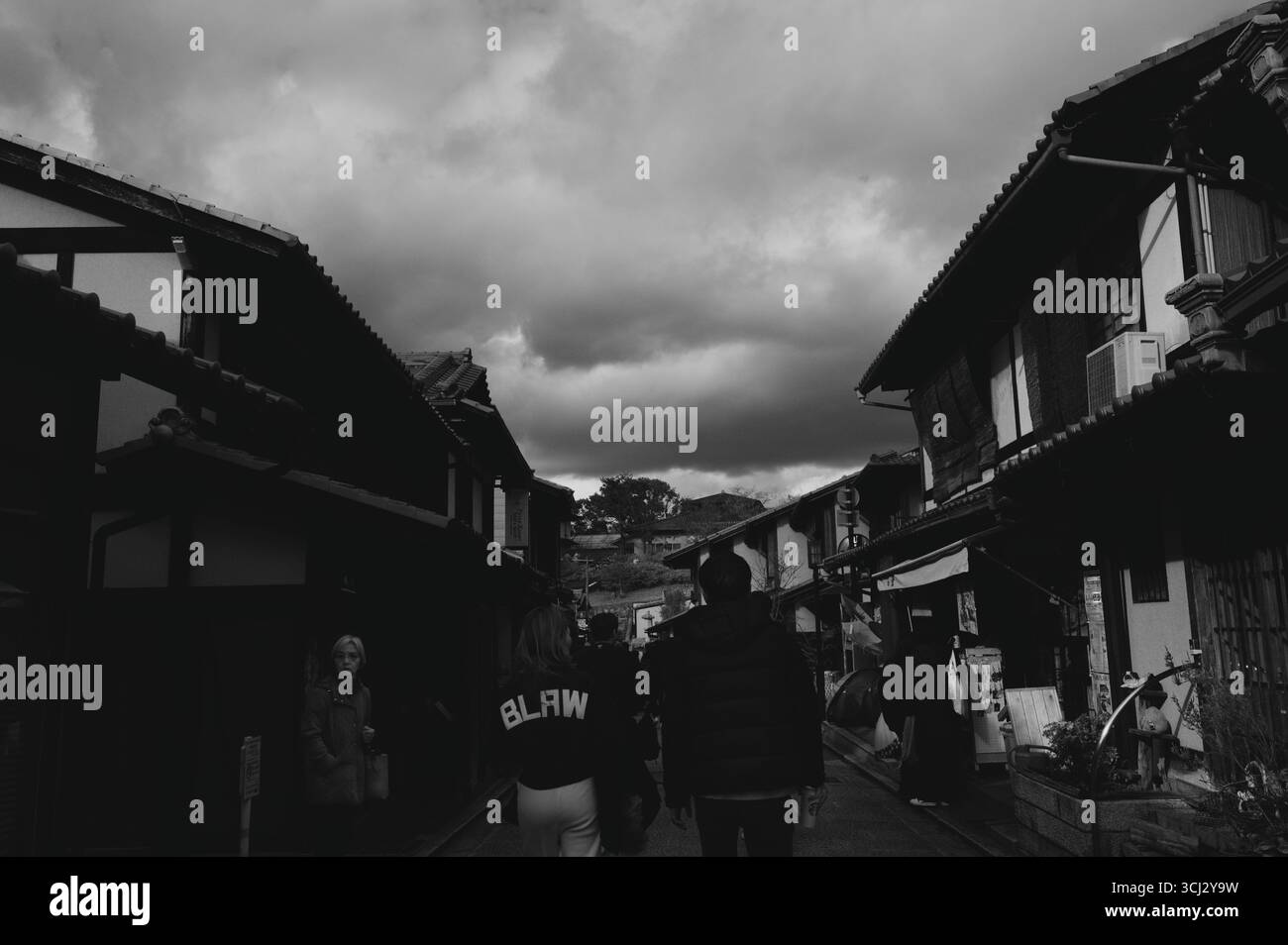 Monochromer Blick auf die Straße im Stadtteil Higashiyama von Kyoto, während Sie zwischen traditionellen Holzhäusern unter einem dramatischen Winterhimmel spazieren Stockfoto
