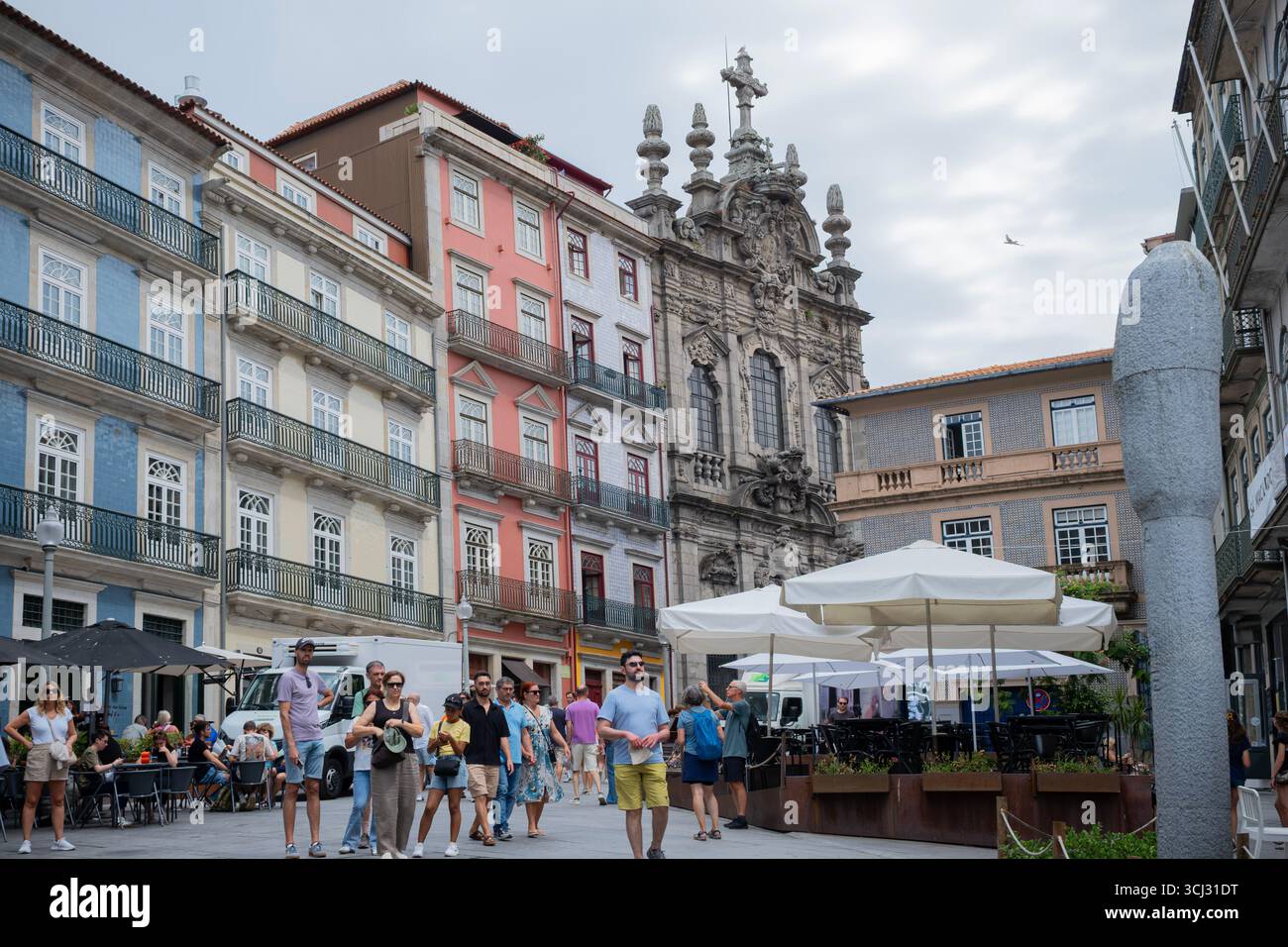 Touristen gehen durch einen belebten Platz in Porto mit farbenfrohen Ziegelgebäuden, Cafés im Freien und der Misericordia-Kirche im Hintergrund Stockfoto