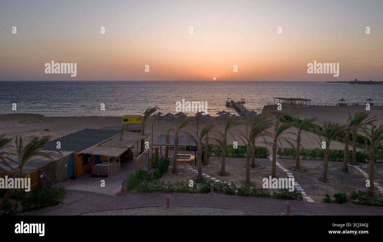 Blick auf den Sonnenaufgang von einem Hotel über den Strand und den Pier, der ins Meer führt. Stockfoto