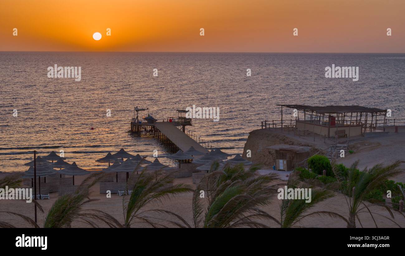Blick auf den Sonnenaufgang von einem Hotel über den Strand und den Pier, der ins Meer führt. Stockfoto