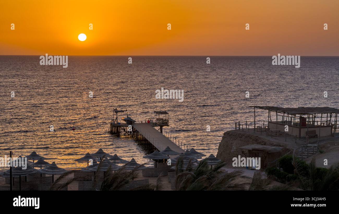 Blick auf den Sonnenaufgang von einem Hotel über den Strand und den Pier, der ins Meer führt. Stockfoto