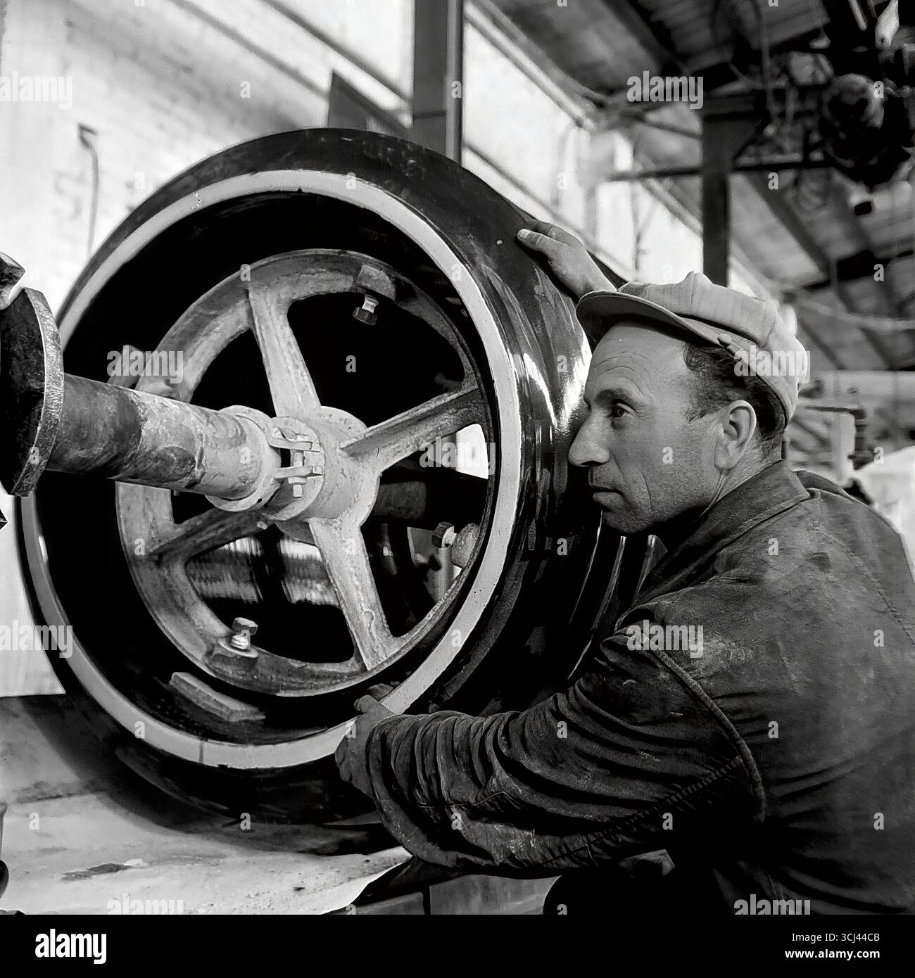 Ein erfahrener sowjetischer Arbeiter in einer Werkstatt in der Isolatorfabrik von Sloviansk arbeitet intensiv an einer Maschine, die Mitte der 1950er Jahre einen großen Teil herstellt Dieses ausdrucksstarke Produktionsprofil im Stil des sozialistischen Realismus verherrlicht den Arbeiter und sein Handwerk und symbolisiert die Macht der sowjetischen Industrialisierung während der Tauzeit. Das Archivfoto fängt die kreative Atmosphäre des friedlichen, industriellen Donbas ein und wird zum Zeugnis der verlorenen Ära der qualifizierten Arbeit vor dem Krieg Stockfoto