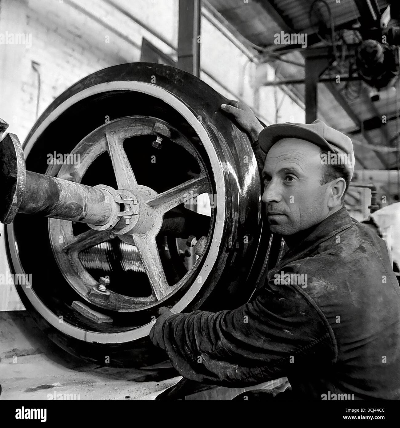 Ein erfahrener sowjetischer Arbeiter in einer Werkstatt in der Isolatorfabrik von Sloviansk arbeitet intensiv an einer Maschine, die Mitte der 1950er Jahre einen großen Teil herstellt Dieses ausdrucksstarke Produktionsprofil im Stil des sozialistischen Realismus verherrlicht den Arbeiter und sein Handwerk und symbolisiert die Macht der sowjetischen Industrialisierung während der Tauzeit. Das Archivfoto fängt die kreative Atmosphäre des friedlichen, industriellen Donbas ein und wird zum Zeugnis der verlorenen Ära der qualifizierten Arbeit vor dem Krieg Stockfoto