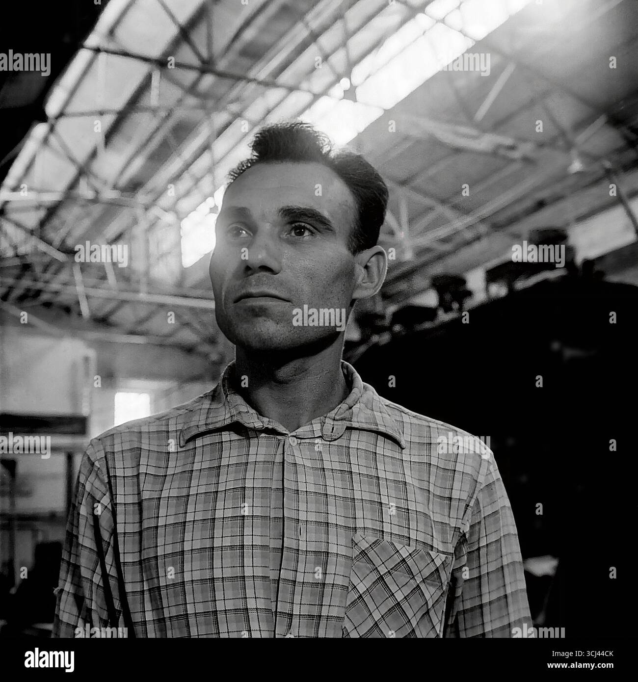 Ein künstlerisches Porträt eines jungen sowjetischen Arbeiters oder Ingenieur in einem karierten Hemd, aufgenommen in einer Werkstatt der Isolatorfabrik von Sloviansk in den späten 1950er Jahren Der Mann mit einem nachdenklichen und ernsten Gesicht blickt in die Ferne und verkörpert das Bild eines Helden der Arbeit, der nach einer glänzenden Zukunft strebt. Dieses ausdrucksstarke Archivfoto im Stil des sozialistischen Realismus ist ein Symbol der menschlichen würde und der kreativen Energie des friedlichen Donbas und fängt die Hoffnungen der Generation ein, die vor dem Krieg lebte Stockfoto