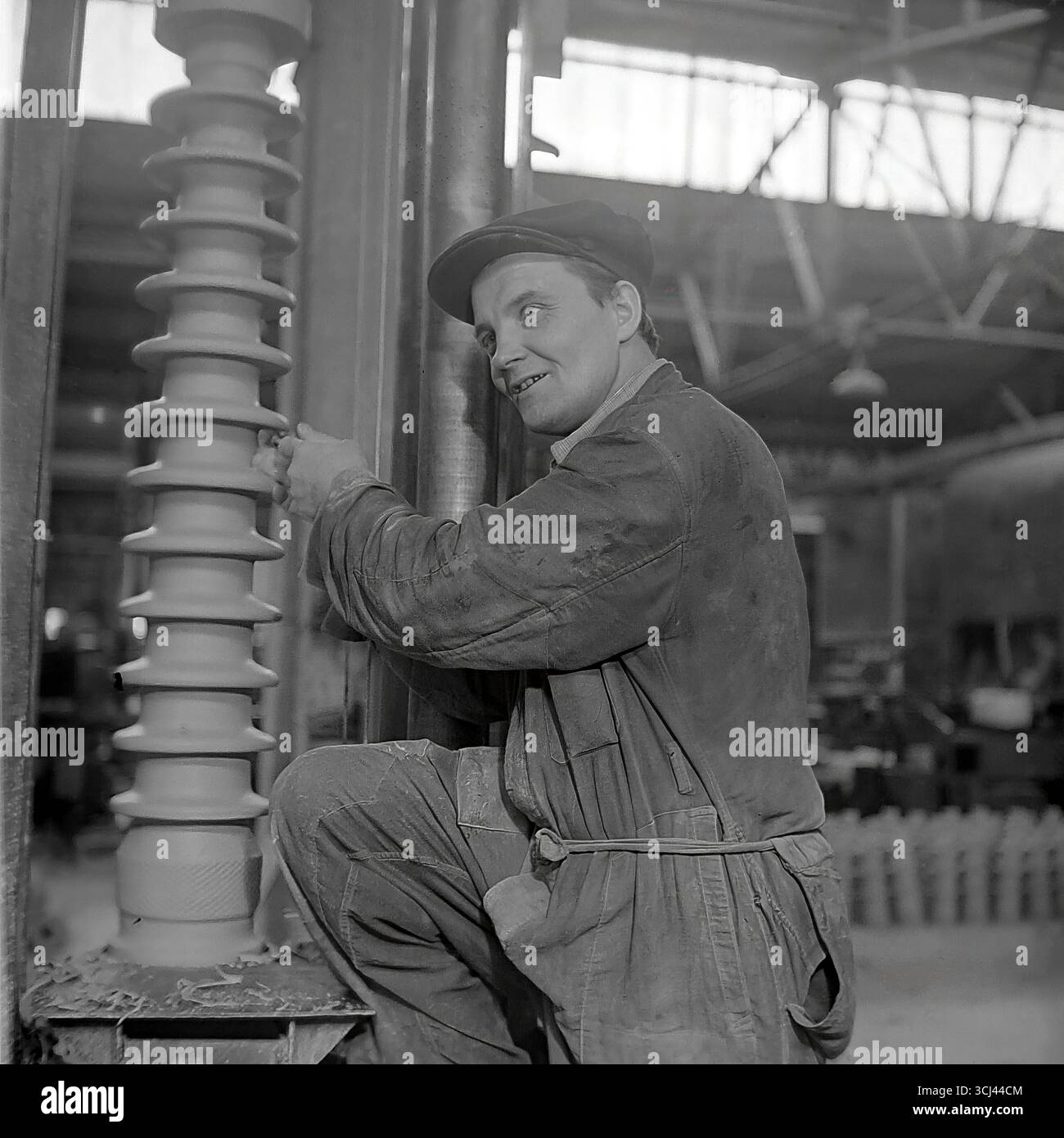 Ein glücklicher sowjetischer Arbeiter posiert mit einem fertigen Hochspannungsisolator in einer Werkstatt im Werk Sloviansk, Ende der 1950er Jahre Das inszenierte Produktionsporträt im Stil des sozialistischen Realismus ist stolz auf sein Werk und der Optimismus der Tauzeit. Diese fröhliche Archivaufnahme ist ein Symbol für das friedliche und kreative Leben im Donbass und fängt die verlorene Ära glücklicher Arbeit vor dem Krieg ein Stockfoto