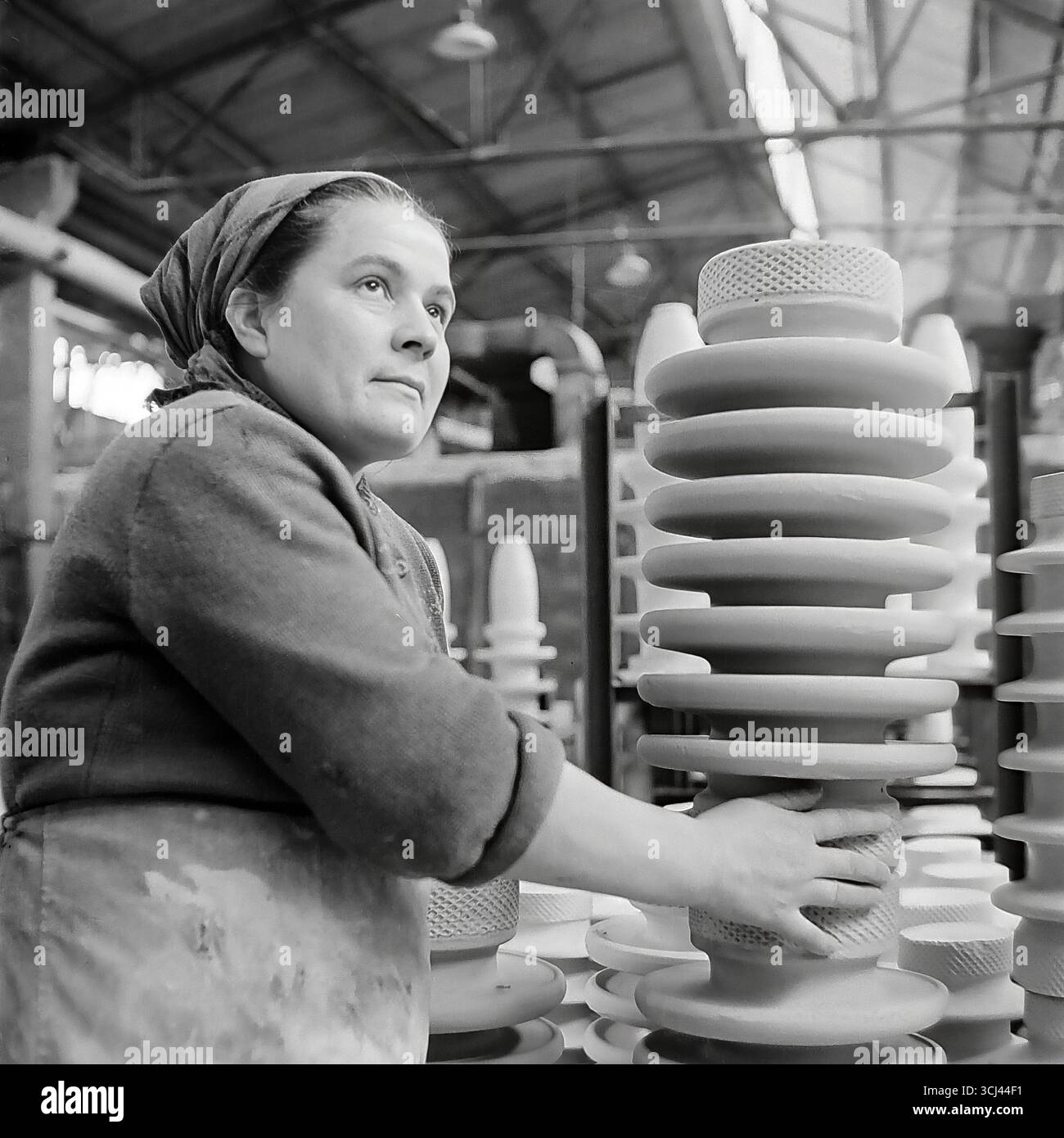 Eine erfahrene sowjetische Arbeiterin mit inspiriertem Gesicht inspiziert Ende der 1950er Jahre in einer Werkstatt im Werk Sloviansk fertige Isolatoren Das Archivporträt eines Arbeiterveteranen im Stil des sozialistischen Realismus vermittelt ein Gefühl der würde und des Glaubens an eine glänzende Zukunft. Dieses Bild einer Weise arbeitenden Frau ist ein Symbol für die kreative Kraft und das friedliche Leben des Donbas und fängt die verlorene Ära vor dem Krieg ein Stockfoto