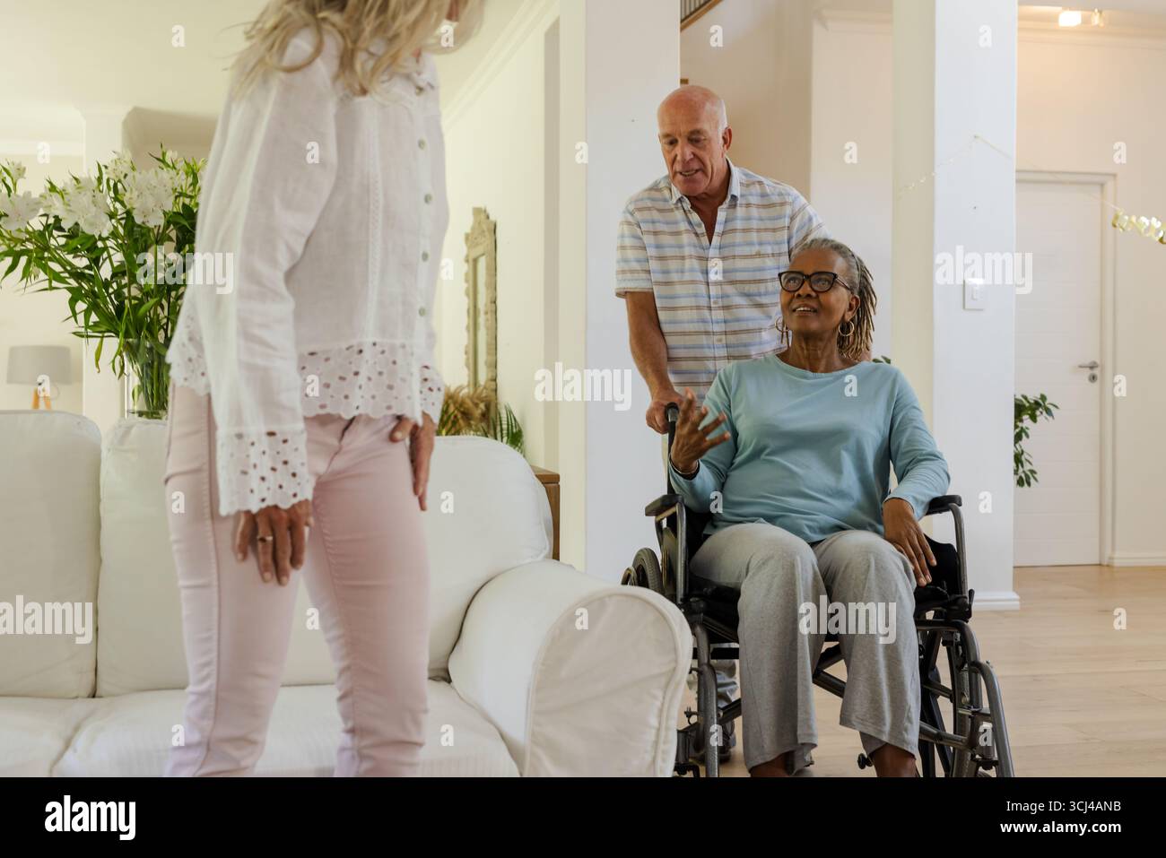 Ältere Freunde, die sich zu Hause unterhalten, eine Frau im Rollstuhl lächelt warm Stockfoto