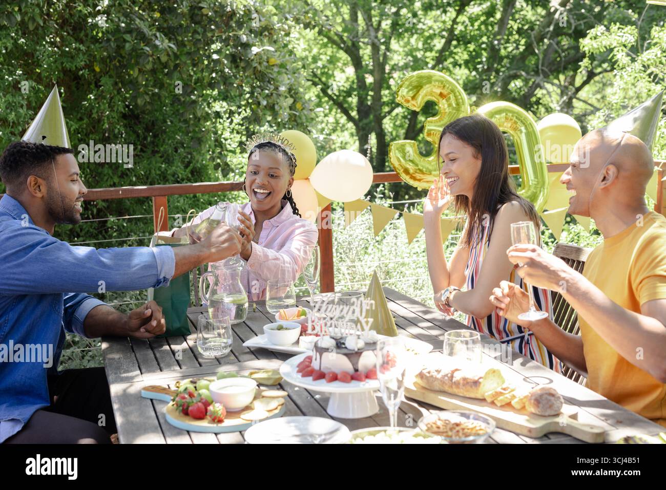 Feiern Sie im Freien Geburtstag, während Freunde mit Champagner unter festlichen Dekorationen anstoßen Stockfoto Feiern Sie im Freien Geburtstag, während Freunde mit Champagner unter festlichen Dekorationen anstoßen Stockfoto