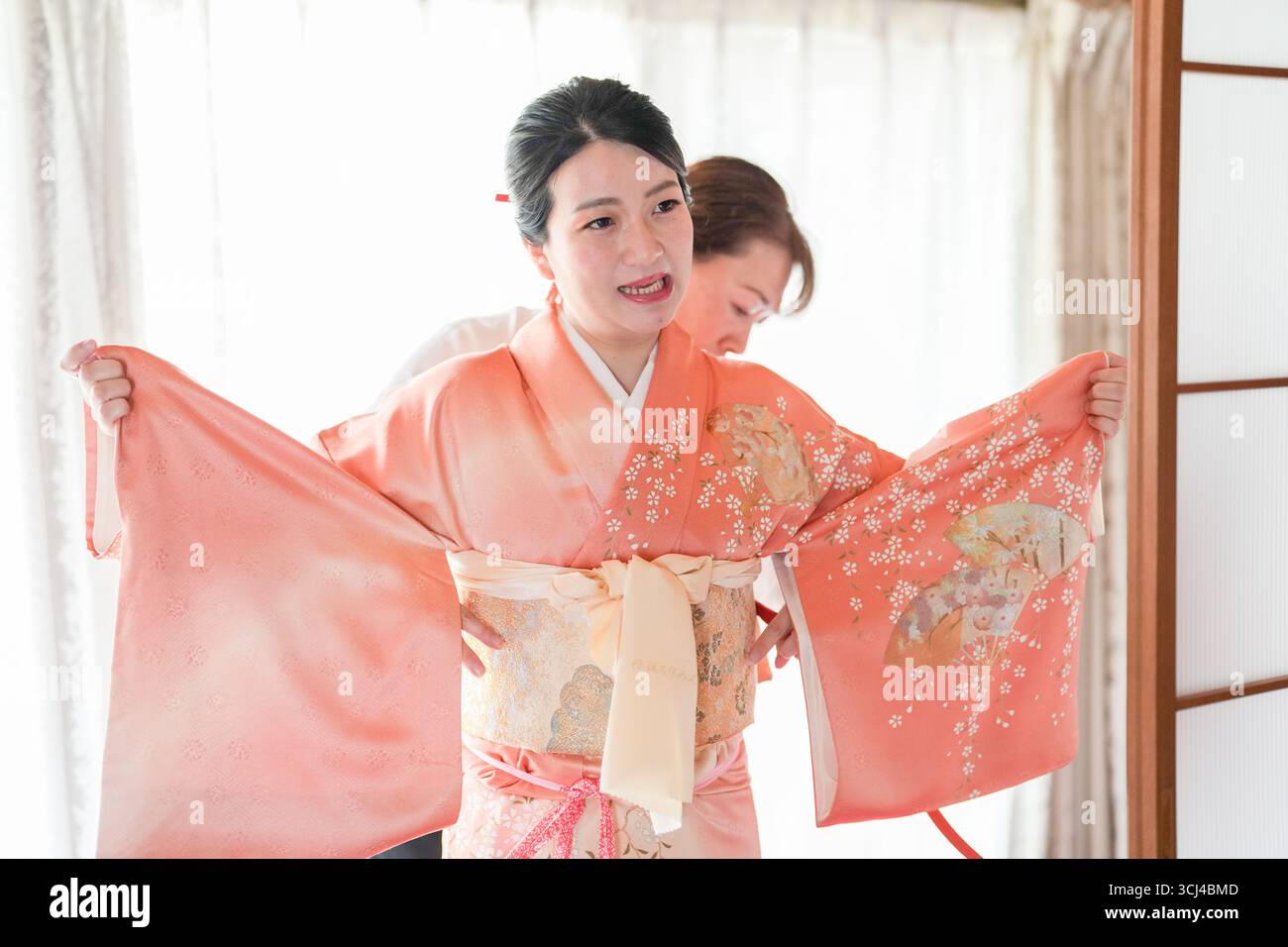 Eine Frau in einem rosafarbenen Kimono passt ihr Outfit an. Sie trägt einen rosafarbenen Kimono und passt ihn so an, dass er richtig passt. Die Frau ist auf dem Laufenden Stockfoto