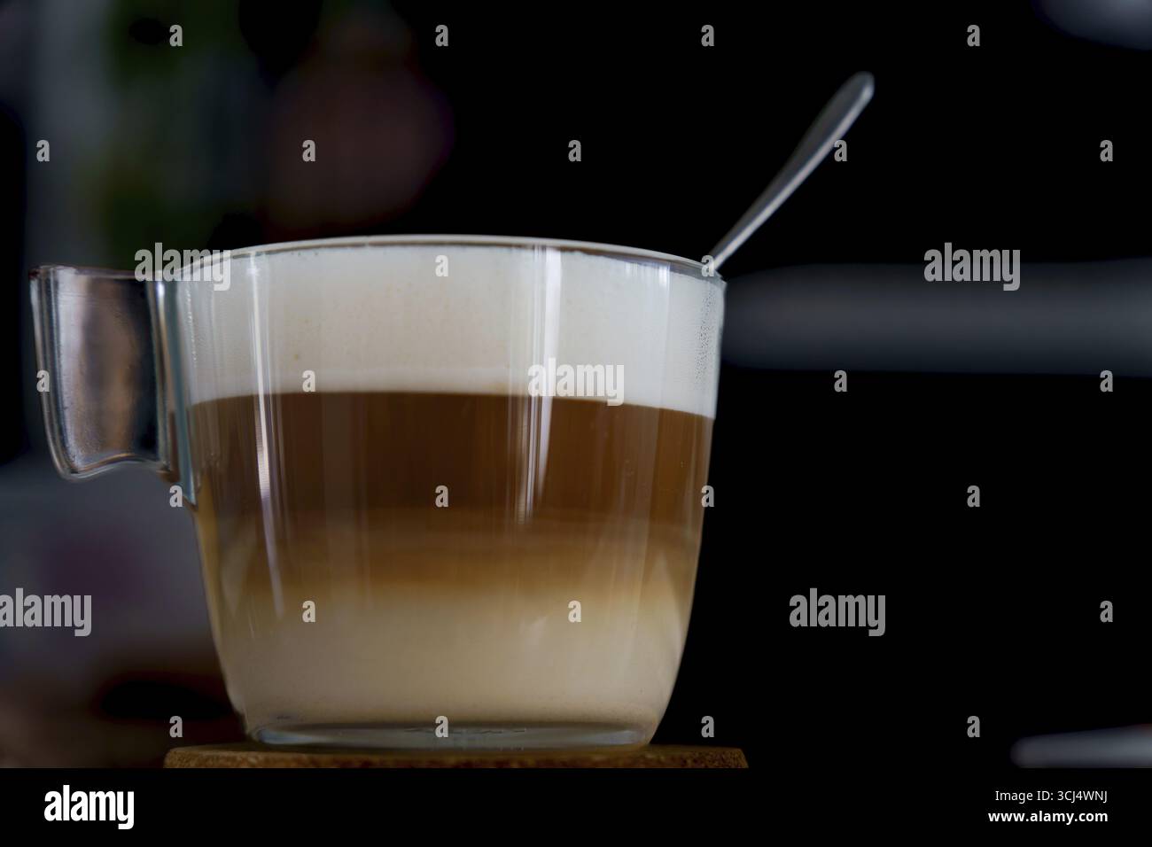 Latte Macchiato in einer Glasschale mit einem Löffel auf dem Schaum, der die unterschiedlichen Schichten Espresso, Milch und Schaum zeigt Stockfoto