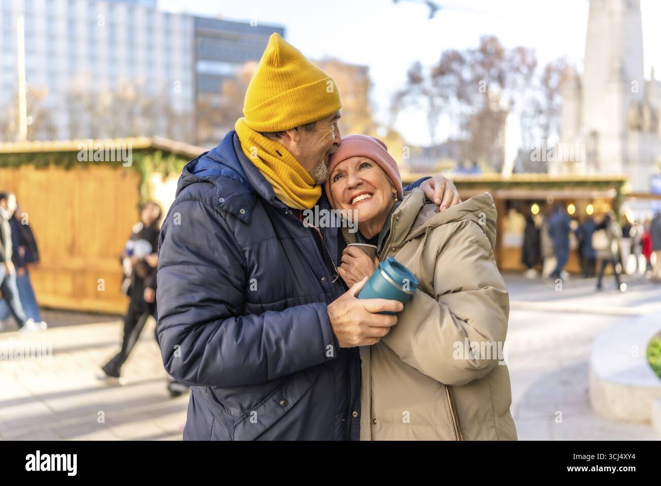 Ein liebevolles Seniorenpaar genießt warme Getränke auf einem weihnachtsmarkt in einer winterlichen Stadt Stockfoto
