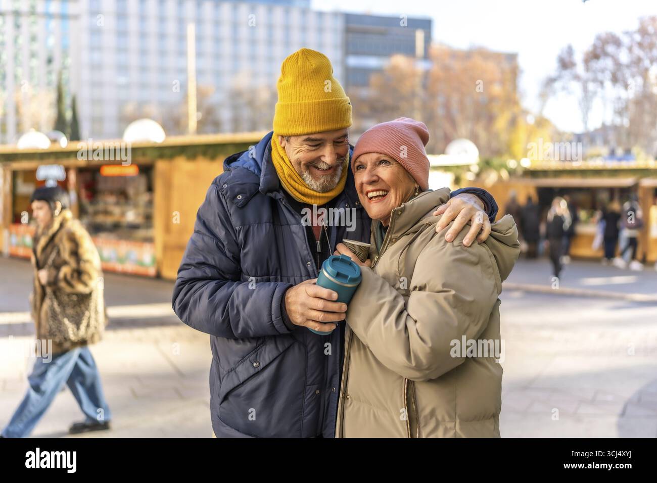 Ältere Ehepaare teilen warme Getränke und genießen die festliche Atmosphäre eines weihnachtsmarktes im Freien, wobei sie fröhlich lächeln Stockfoto