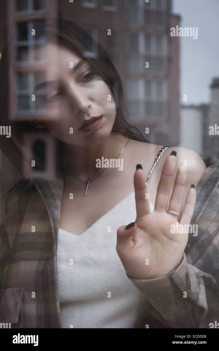 Traurige einsame junge Frau, die durch das Fenster auf die moderne Stadt blickt Stockfoto