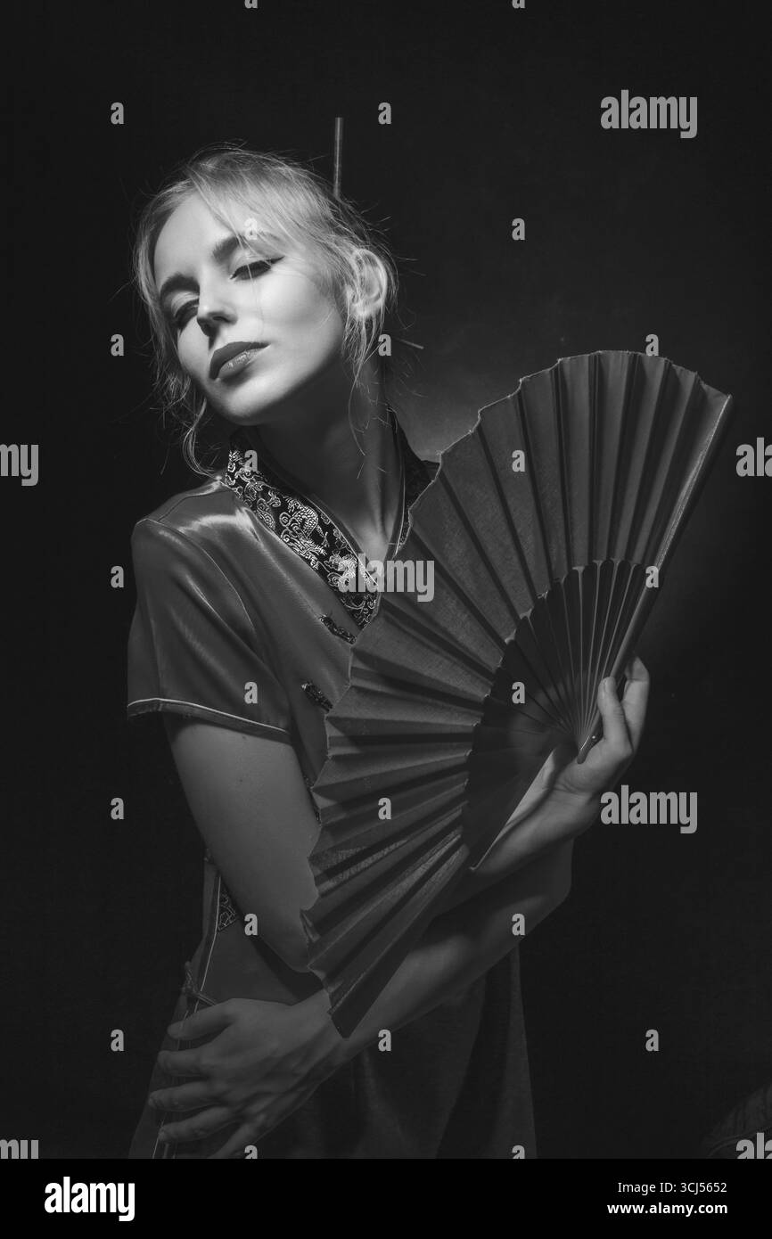 Mädchen in asiatischem Kleid mit rotem Fan auf schwarzem Hintergrund, monochrom Stockfoto