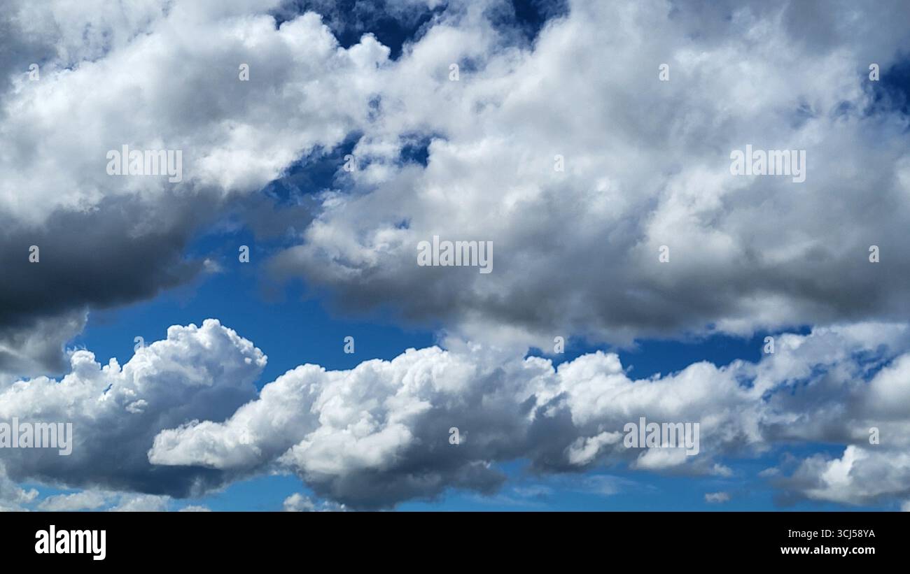 Wolkenformationen mit starken Kontrasten und verschiedenen Schattierungen von weiß und Grau bis fast schwarz über blauem Himmel Stockfoto