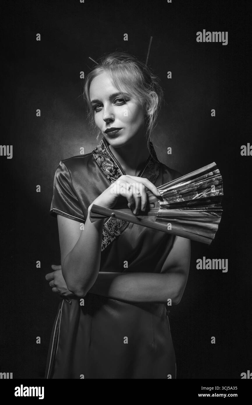 Mädchen in asiatischem Kleid mit Fan auf schwarzem Hintergrund, monochrom Stockfoto
