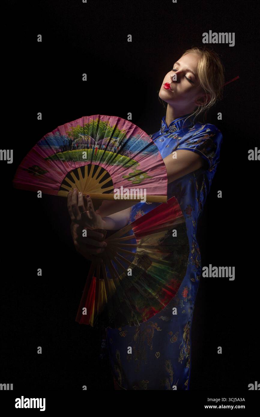 Mädchen in japanischem Kostüm, das mit Fans auf schwarzem Hintergrund tanzt Stockfoto