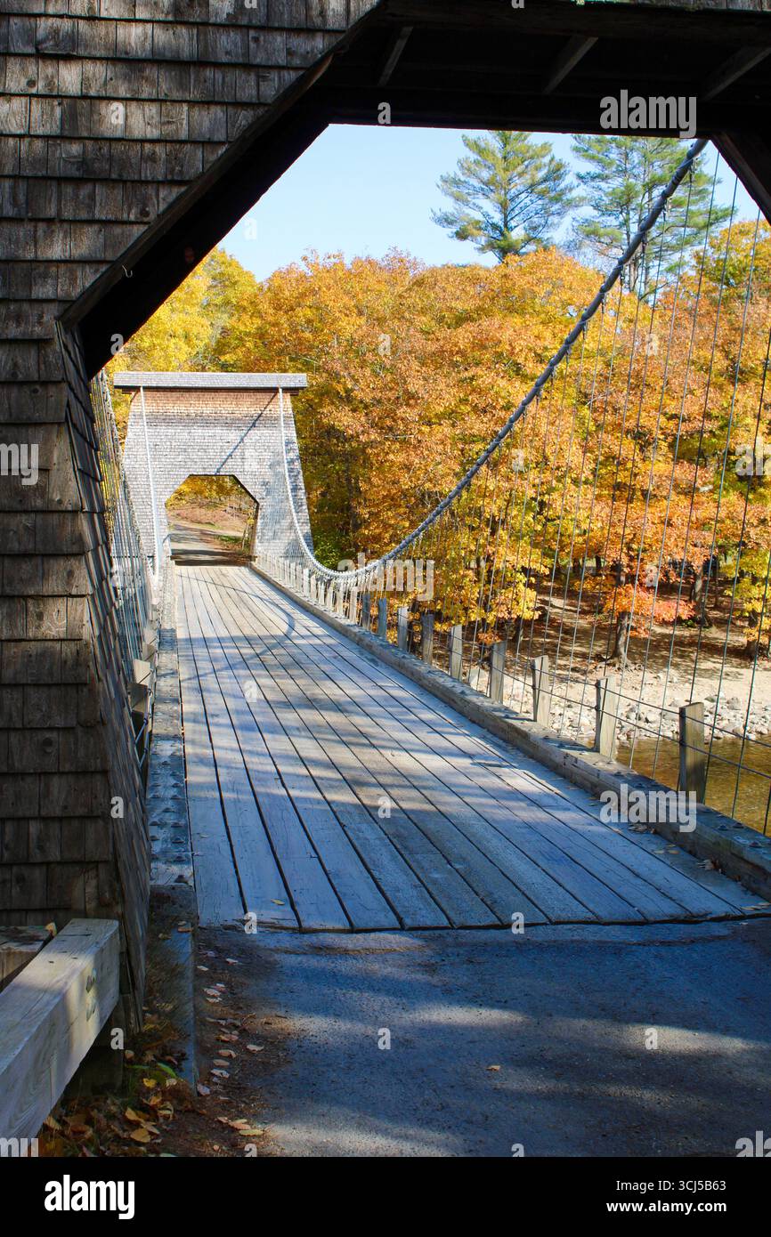 Malerische Drahtseilbrücke über einen Fluss in Maine umgeben von Herbstlaub Stockfoto