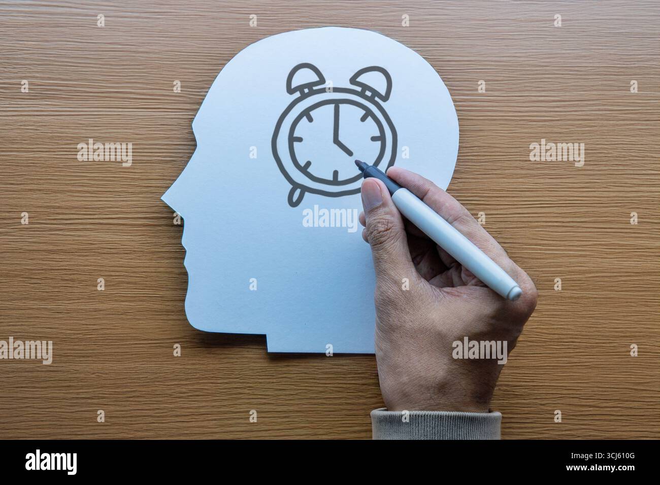 Ein kopfförmiger Ausschnitt mit einer Hand, die einen Wecker zeichnet. Zeitmanagement, mentale Organisation und Selbstdisziplin. Stockfoto