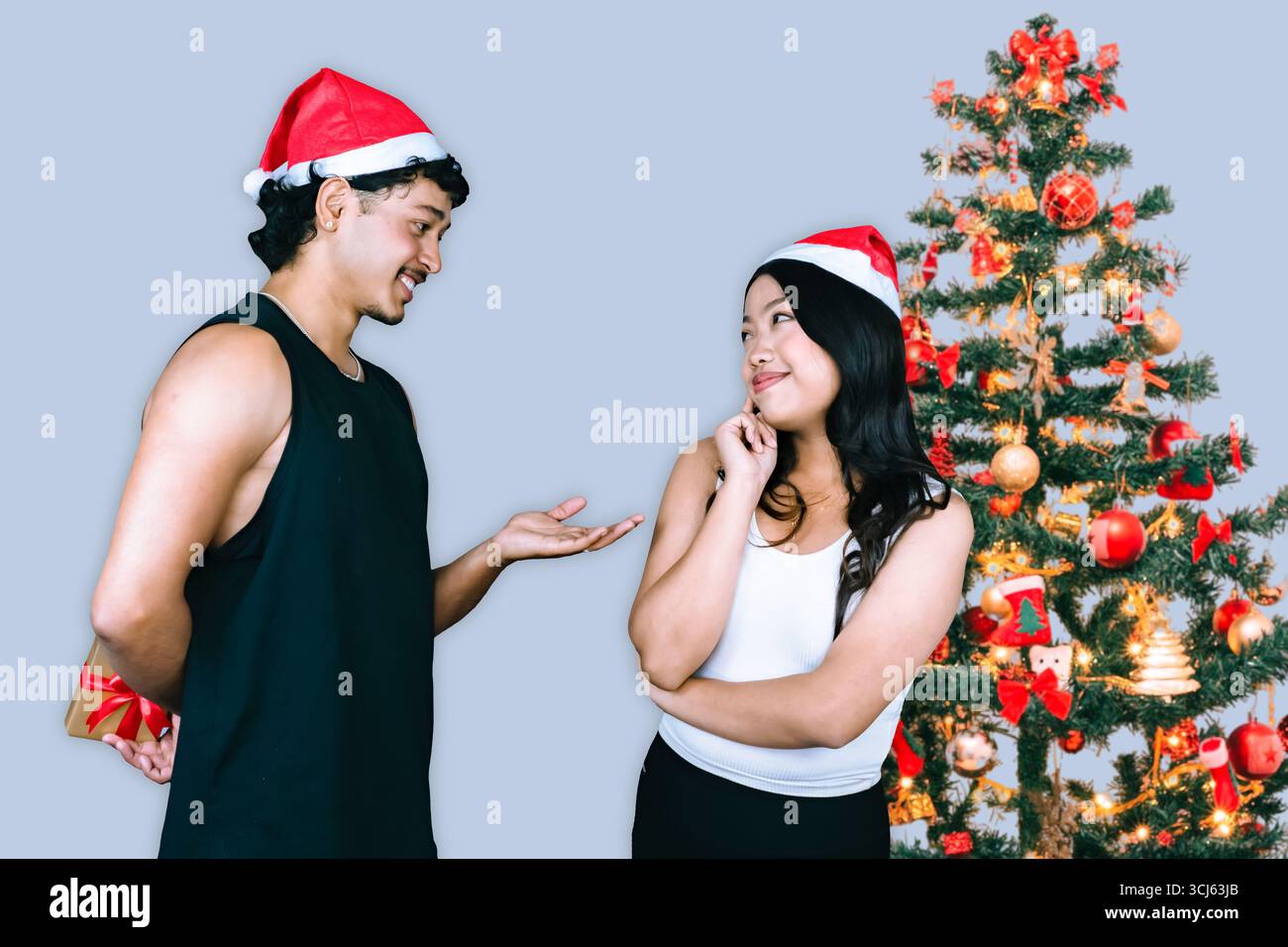 Passen Sie männliche und weibliche Athleten, die vor einem Weihnachtsbaum stehen, mit Fitnessgeräten und Geschenken, um die Weihnachtszeit zu feiern und gleichzeitig Kraft zu zeigen Stockfoto