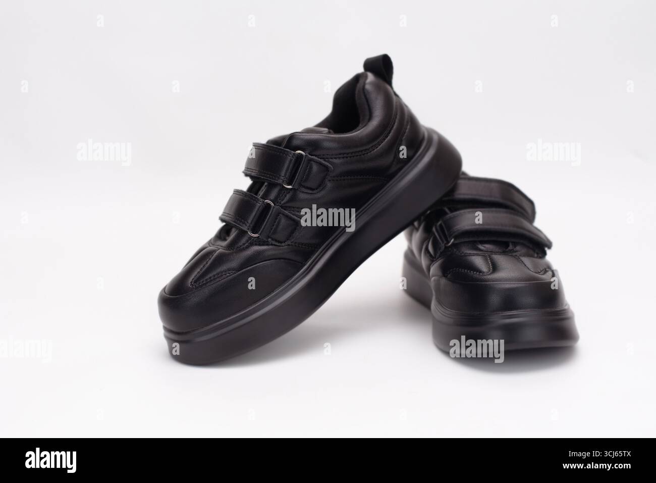 Ein Paar schlanke schwarze Sneakers mit Klettverschlüssen, die Style und Tragekomfort auf weißem Hintergrund bieten. Ideale Schuhe für Freizeit Stockfoto