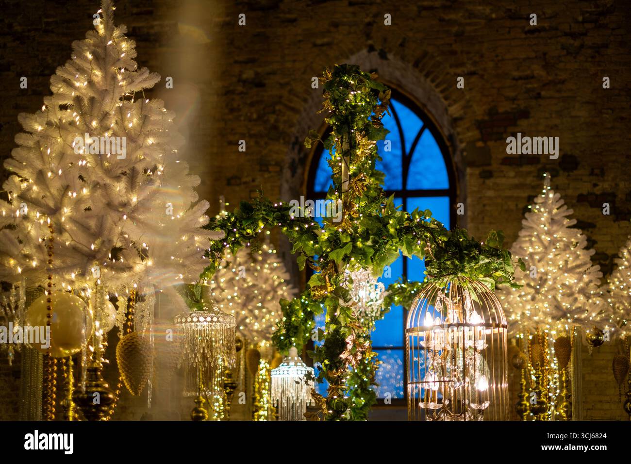 Die Weihnachtsdekoration mit weißen Bäumen und einem atemberaubenden Kreuz wird beleuchtet, was eine festliche Atmosphäre in einer Kirche schafft, die das festtagsgespenst unterstreicht Stockfoto