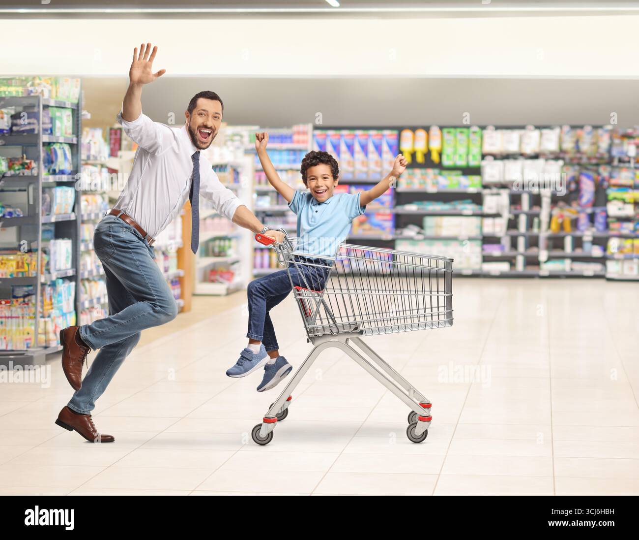 Vater rennt in einem Supermarkt und fährt einen glücklichen Jungen in einem Einkaufswagen Stockfoto